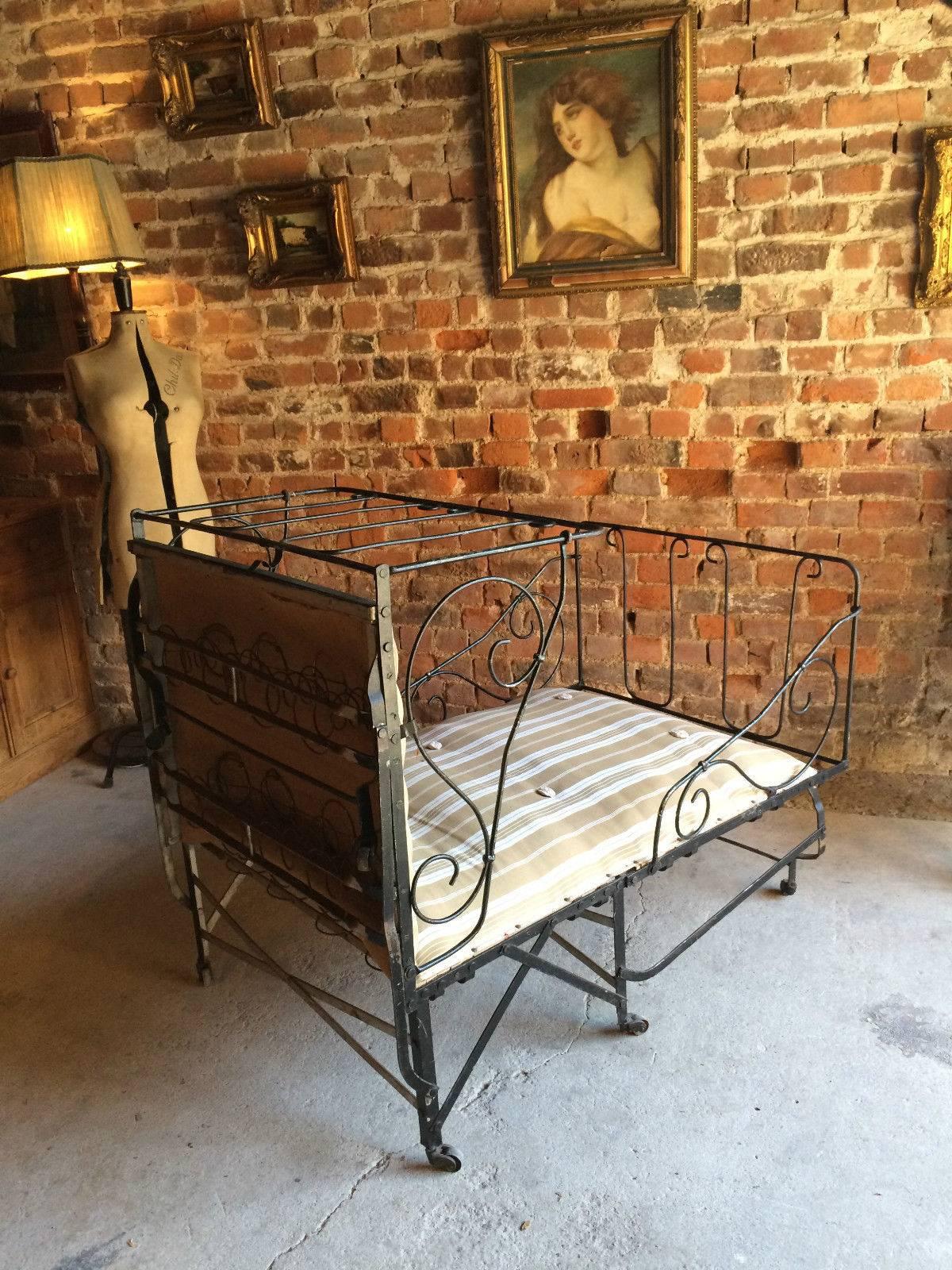A French antique floor standing campaign day bed, striped sprung mattress with scrollwork detail and standing on raised legs with casters, folds down easily.