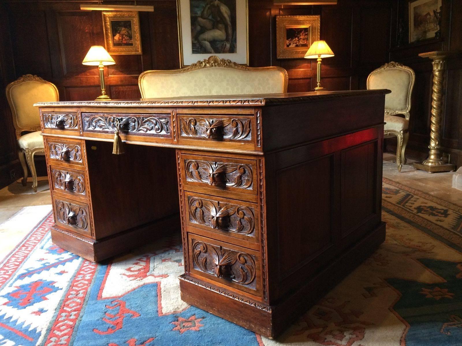 Antique 19th century 'Green Man' Walnut partners desk in the Flemish manner, the oxblood gilt tooled leather inset top over an arrangement of twelve drawers and two cupboard doors (one with campaign style drawers within) with carved masks and