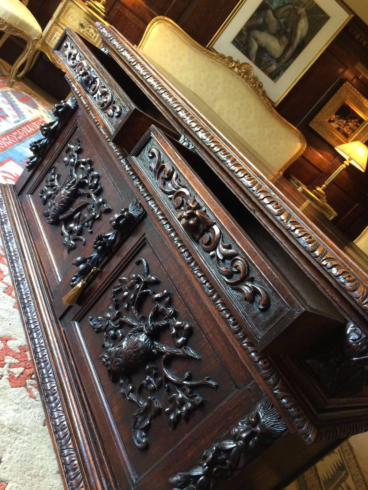 A heavily carved 19th century French 'Green Man' solid oak sideboard credenza, rectangular two plank top above two frieze drawers, over two heavily carved paneled cupboard doors featuring hanging game, raised on casters, comes with key with and
