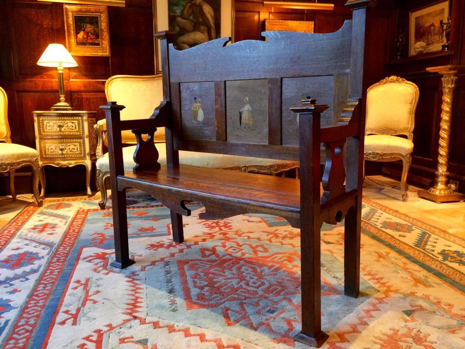 A Victorian Arts & Crafts oak inlaid hall settle bench. The bench with Flemish marquetry inlaid details to the fielded panels in the manner of Rowley Gallery set over a planked bench with shaped elbow supports being raised on squared legs with pad