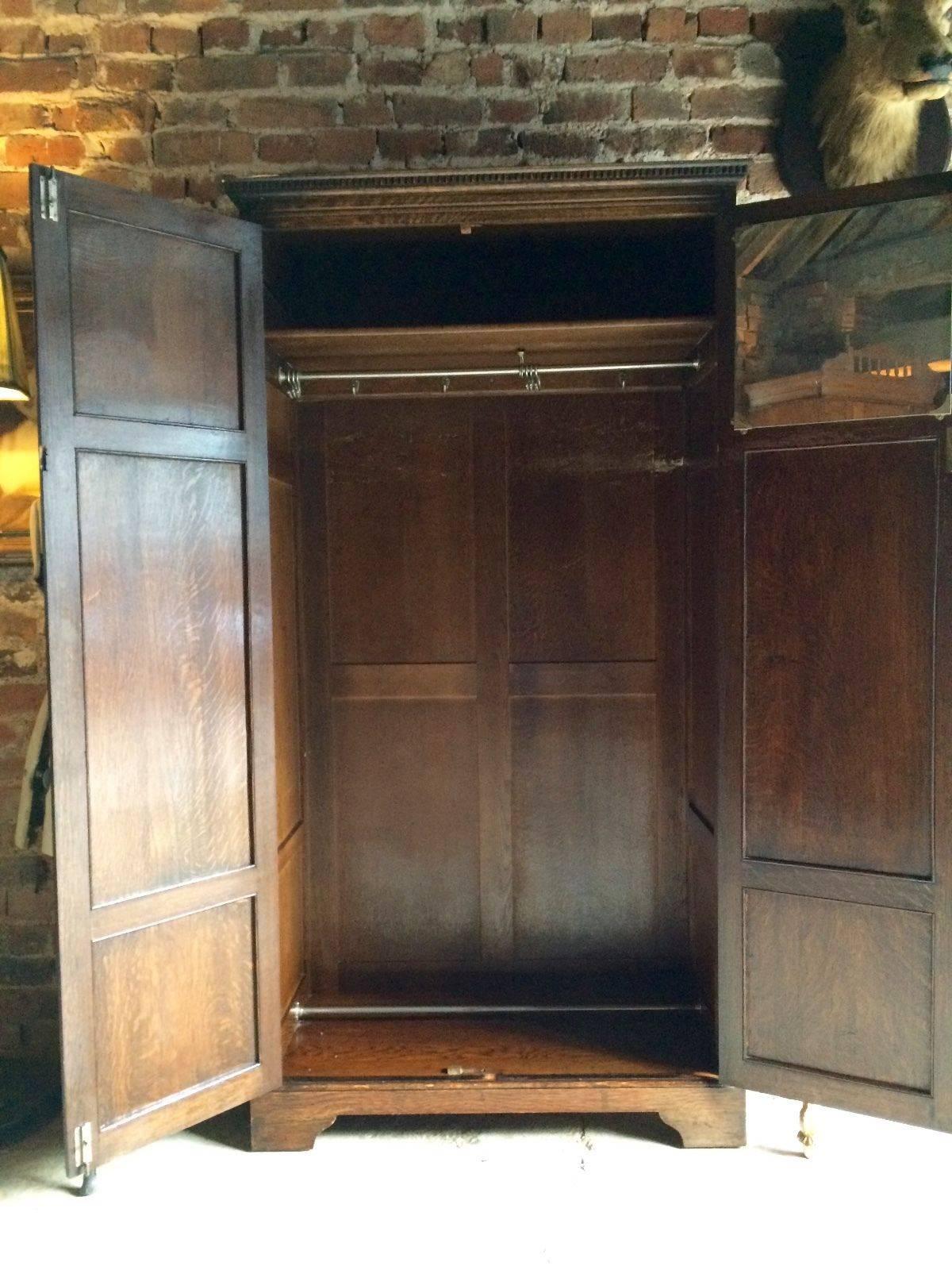 A gorgeous early 20th century 'Gothic' style solid oak two-door wardrobe, the moulded dentil cornice over two quarter fielded panel doors with English carved rose panels inset atop, enclosing hanging rail, shoe rail and small mirror to door, raised