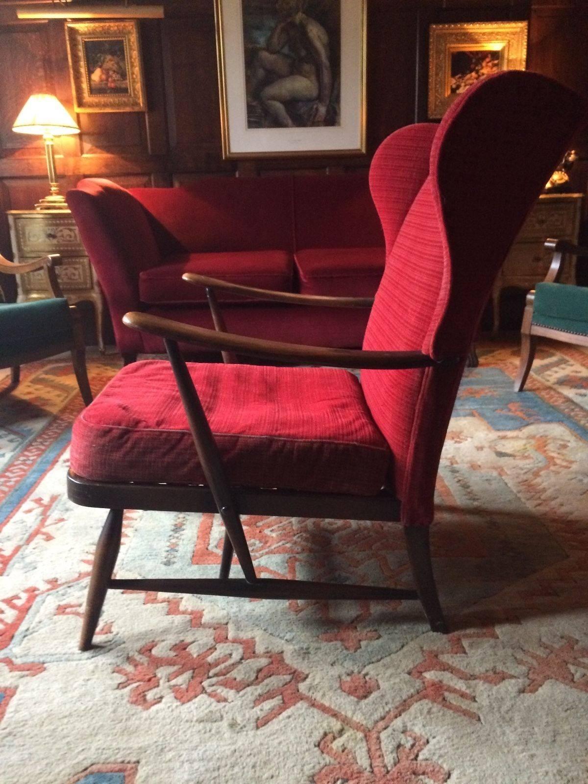 A fabulous Danish design Mid-Century 1950s original Ercol wingback armchair, the chair with original red cushions with high wing backs and shaped and carved elbow rests, ideal for reupholstery, personally I would leave as is.