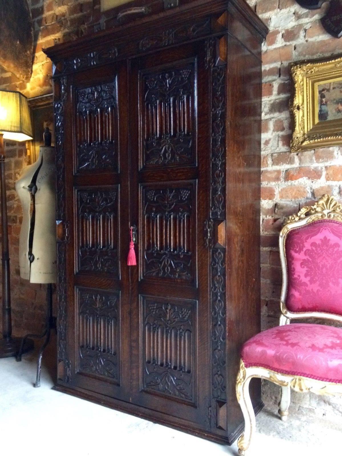 A stunning and very imposing profusely carved Edwardian Gothic taste oak wardrobe armoire circa 1905, carved cornice top over a pair of fielded panelled doors with extensively carved tri-sectional panels decorated with linen fold, grape vine and