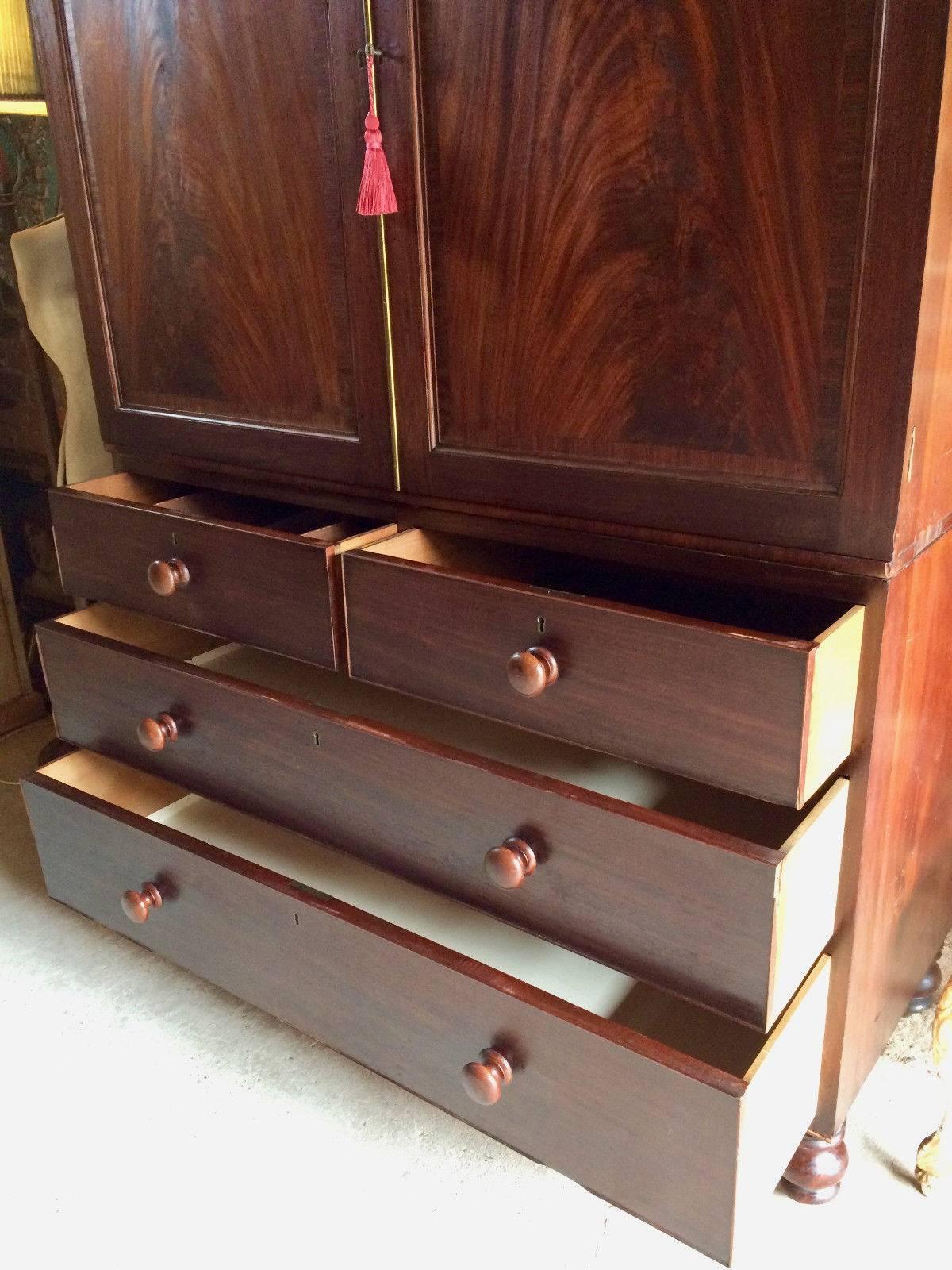 A very tall and handsome antique 19th century Victorian solid mahogany clothes press, the top with moulded cornice above two panelled doors, enclosing six mahogany sliding trays, the base with two short and three panelled drawers all with turned