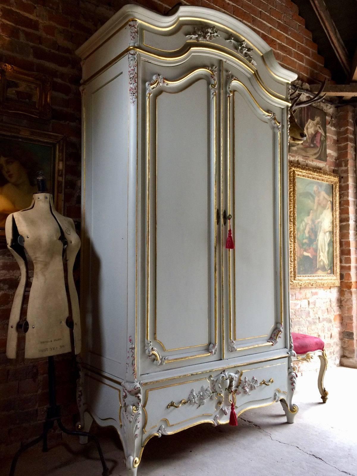 A magnificent and extremely beautiful French gilt and painted armoire of tall proportions, the arched corniced pediment over twin panelled doors each with full length mirrors to the inside, with brass hanging rail, over single drawer base and raised