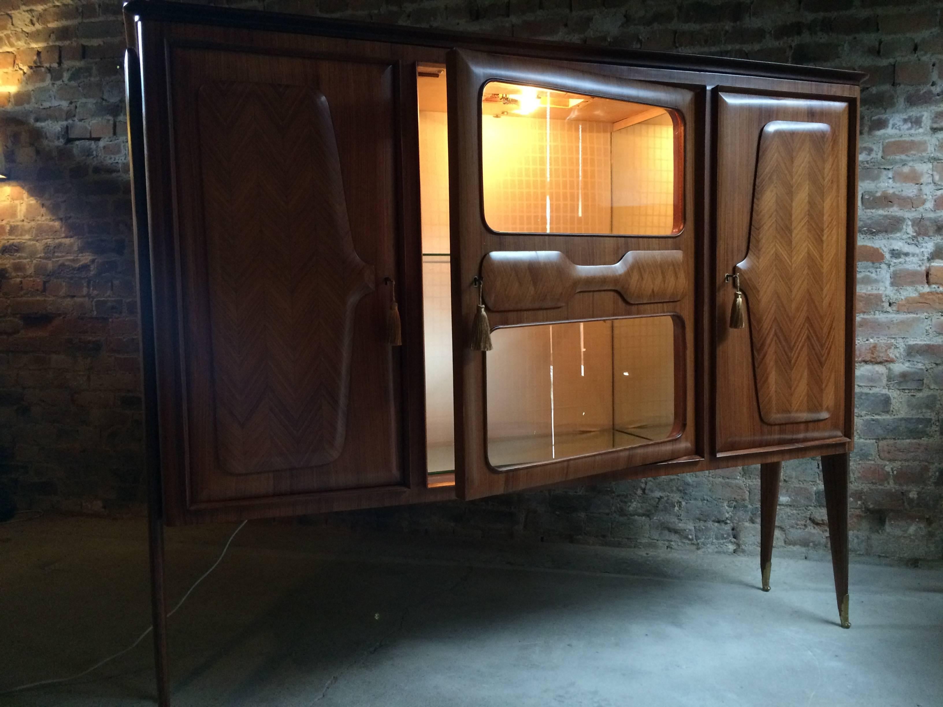 An Italian Mid-Century walnut bar cabinet dating from 1950s, designed by Vittorio Dassi (Milan, 1893-1973). It features two sycamore lined cabinets flanking an illuminated central glazed and mirrored section with glass internal shelves and working