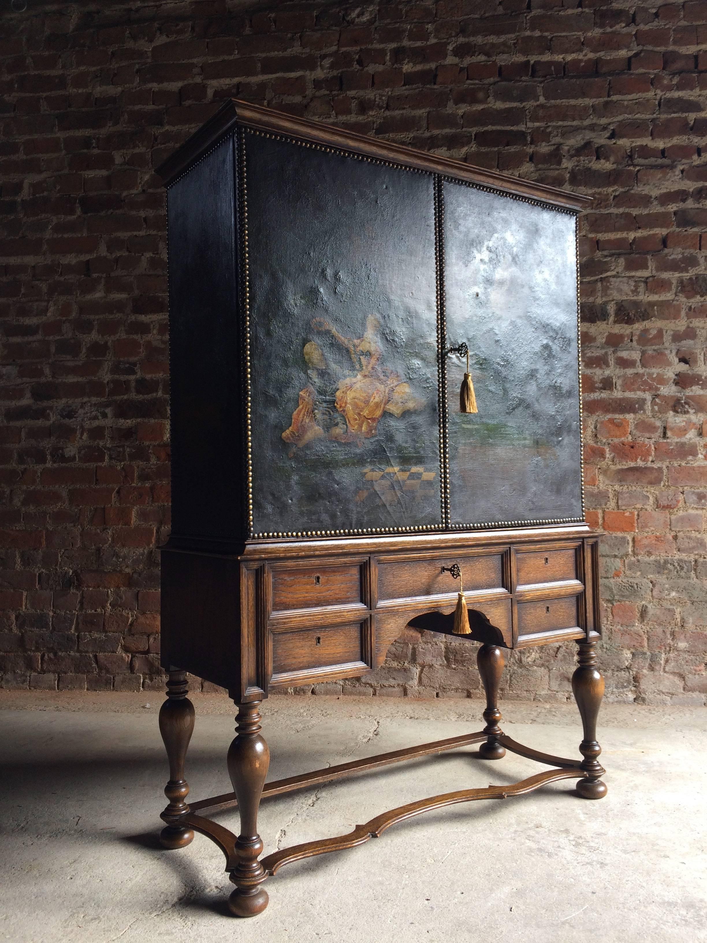 An unusual early 20th century solid oak cocktail cabinet, the canvas covered upper section painted with classical figures in a rural landscape, the two canvas covered doors with golden glass mosaic interior, glass shelves and two internal lights,