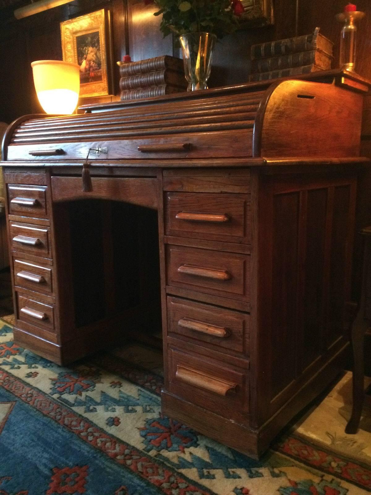 A gorgeous and original large antique solid oak twin pedestal roll top desk, with small drawer and various pigeon holes to the writing area, the desk having a central frieze drawer and seven drawers to the right and left, with lock and working key