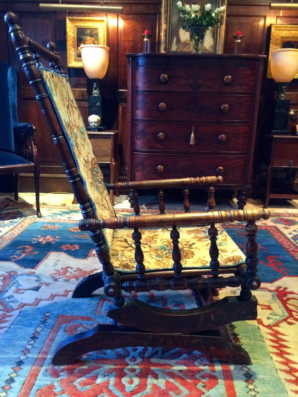 A late 19th century Victorian mahogany American rocking chair armchair with bobbin spindles to the arms and frame, upholstered in a ‘Floral’ woven material, sitting on sprung legs allowing a gentle rocking motion, the armchair is extremely