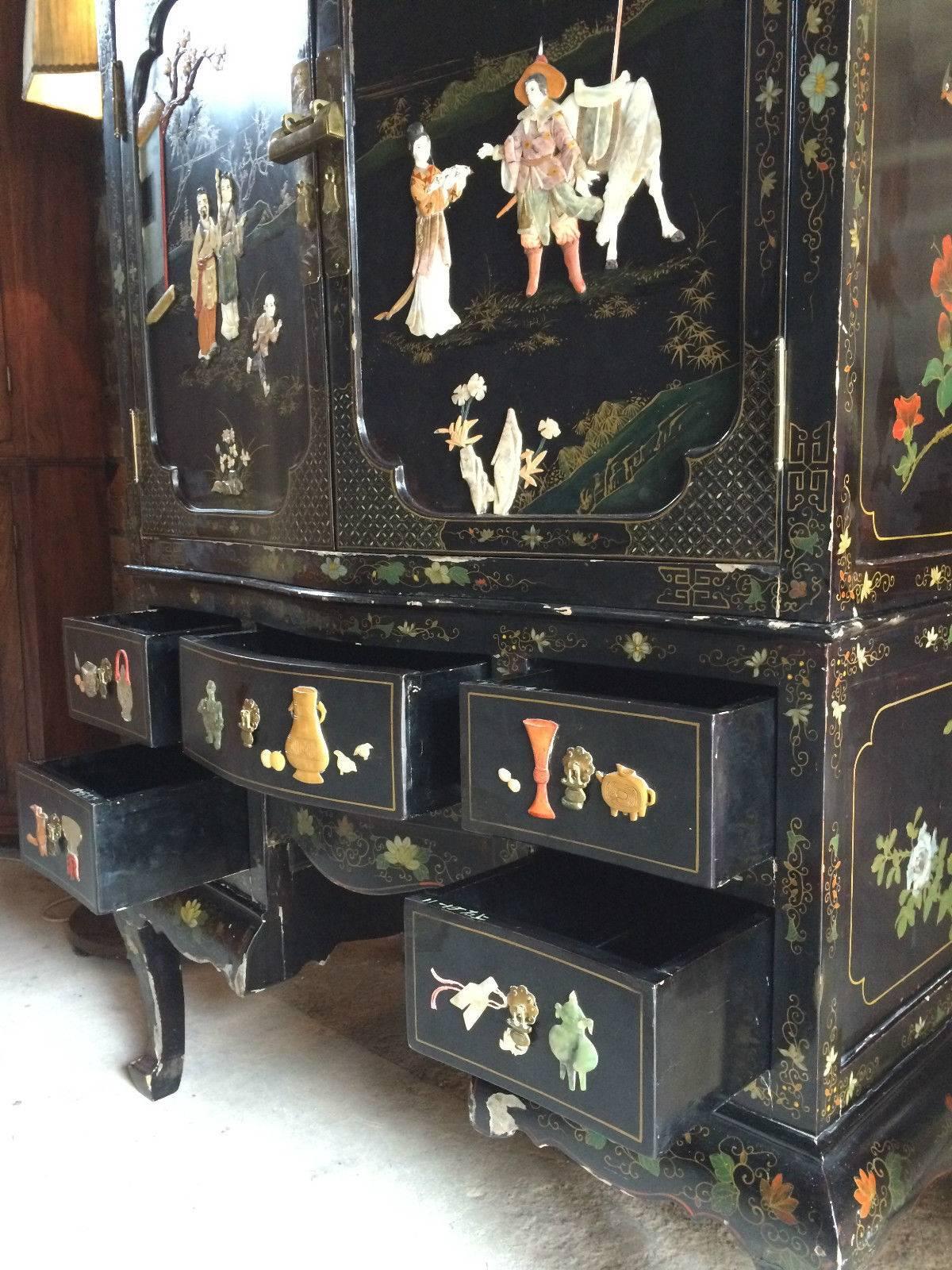 A beautiful heavily decorated chinoiserie black lacquered oriental ebony cabinet over chest, the ornately decorated upper section with a pair of panelled doors with oriental brass lock with large interior, the lower section with long central frieze