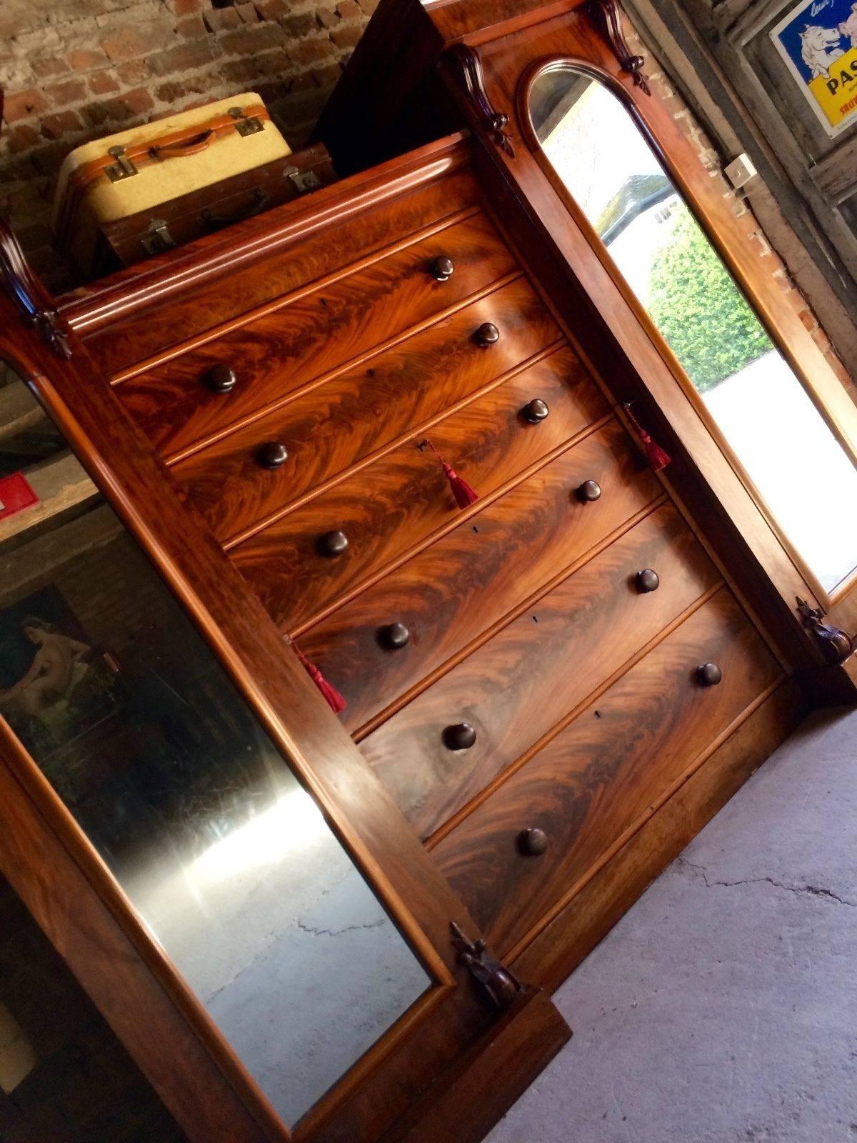 A breathtakingly beautiful, large and imposing antique 19th century Victorian flamed mahogany compactum wardrobe, circa 1850, two arched and mirrored wardrobe sections with projecting corniced tops with hanging rail and hooks, the interiors have