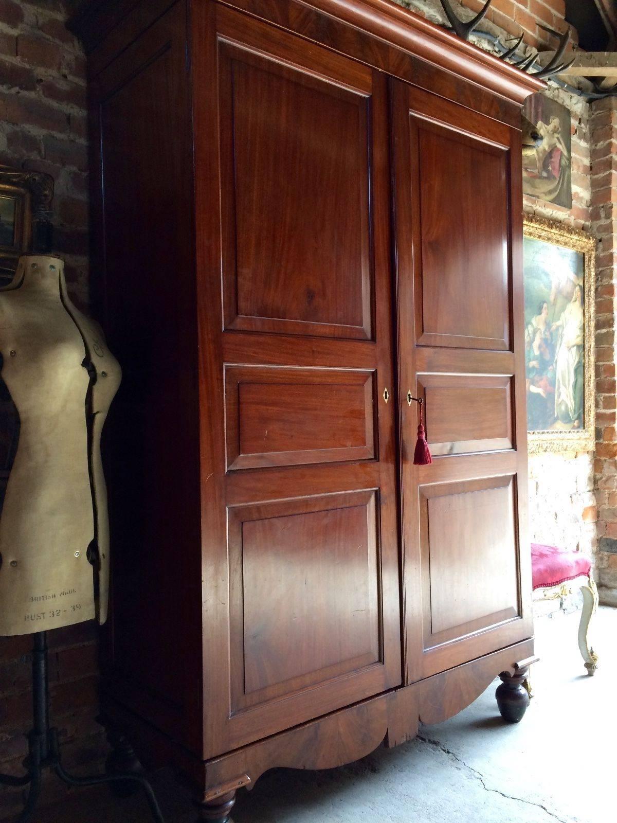 A tall 19th century Victorian flamed mahogany two door wardrobe, corniced top over two panel doors enclosing cloth lined interior with hanging rail raised on a stand with four turned legs, comes with one working key with tassel, the wardrobe