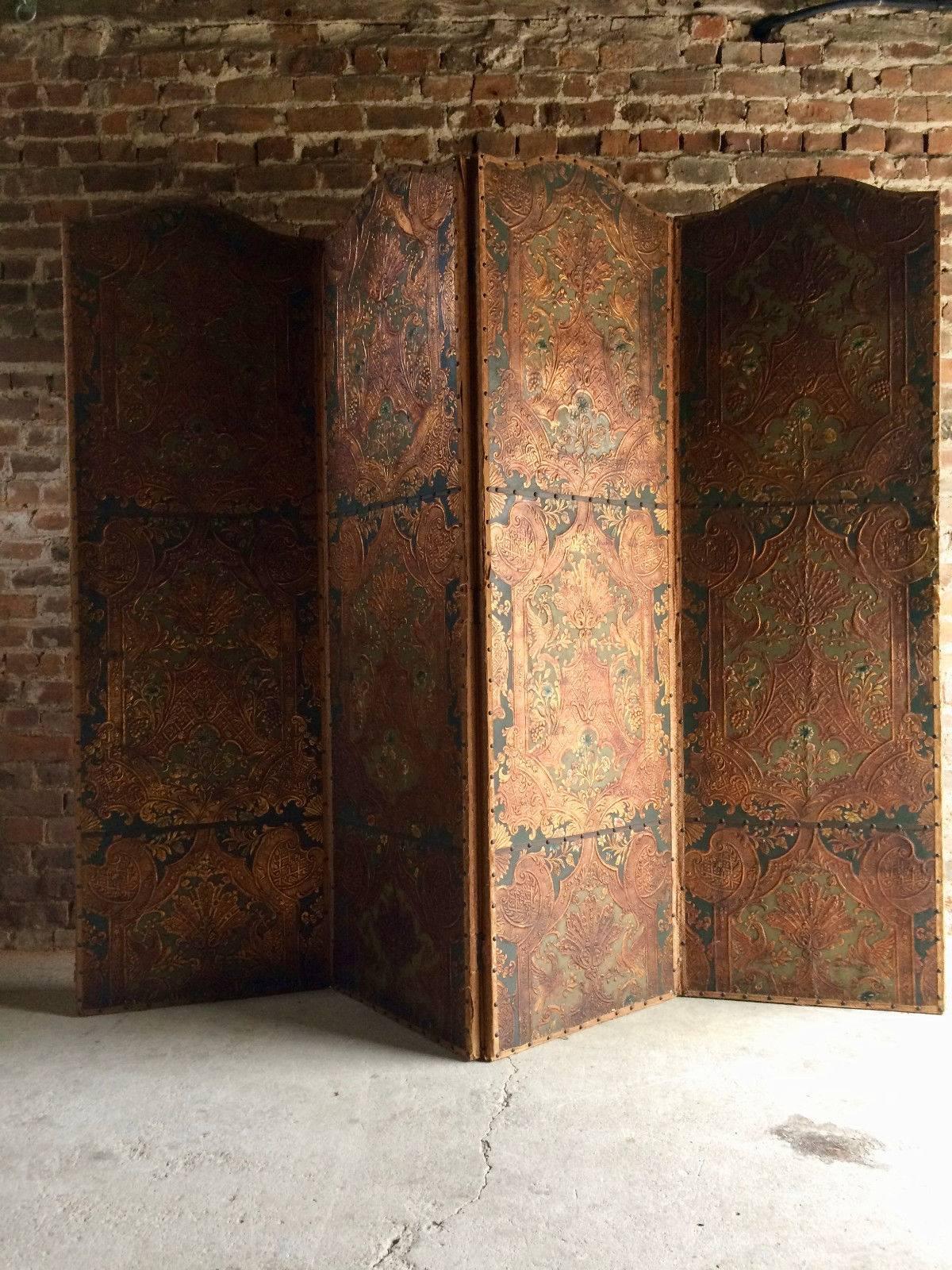 A stunning antique 19th century continental heavily embossed leather four fold dressing screen or room divider, the screen with four folding leather panels all classically embossed with shades of reds, greens, and golds, the reverse the with