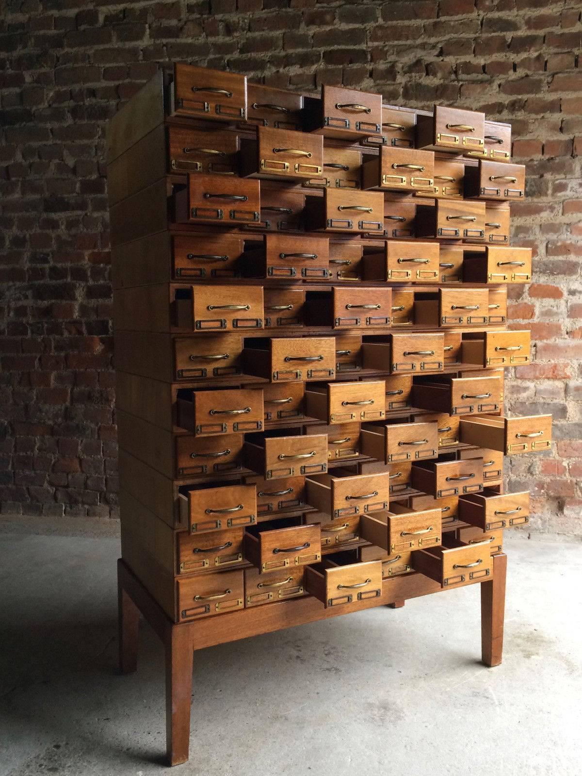 A magnificent mid-20th century haberdashery Industrial oak stacking office chest cabinet, having a bank of sixty six drawers each with brass index card holder, raised on a base with square section supports, the eleven drawer sections each stack on