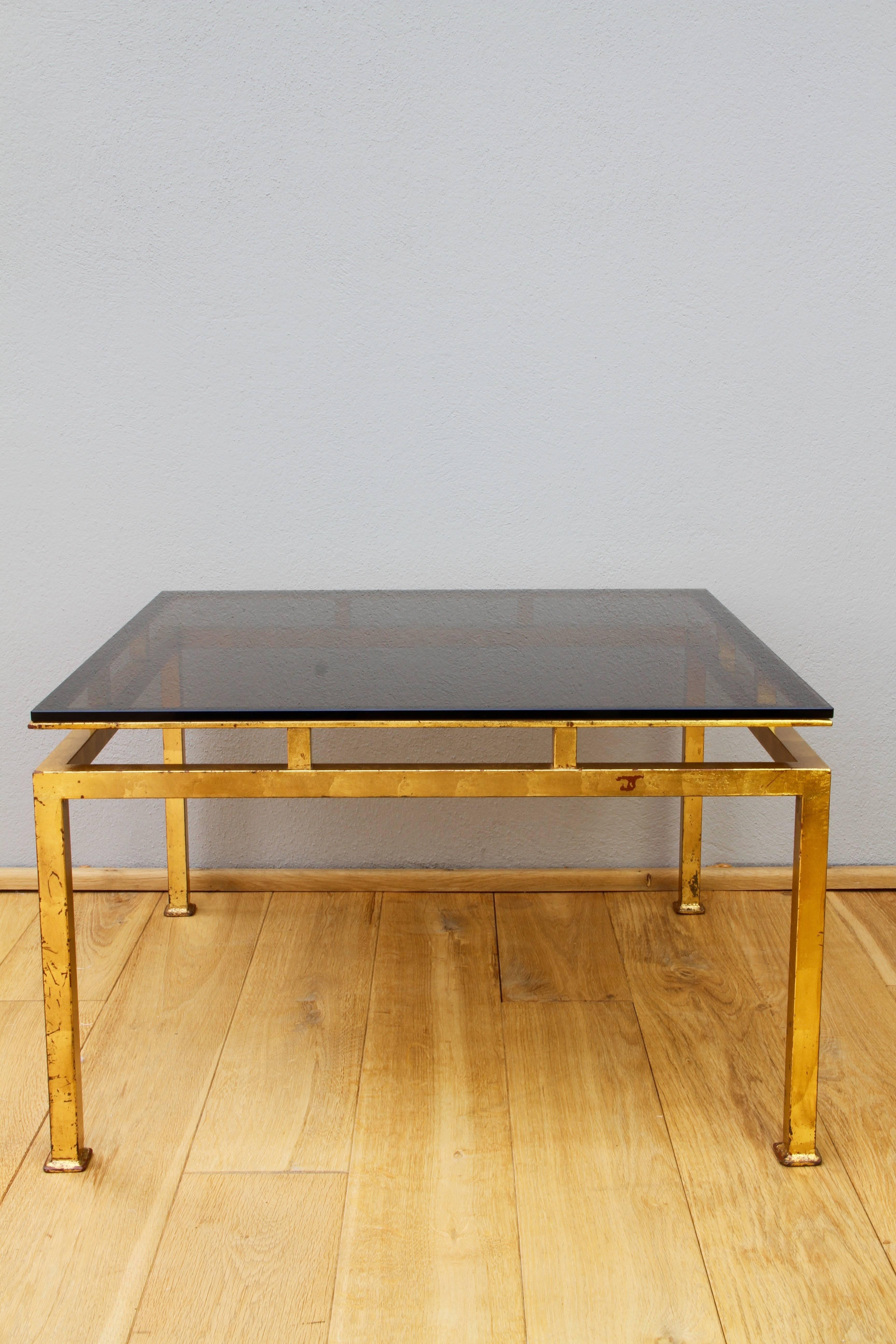 A large pair of French or Italian square Gilt iron coffee tables with thick smoked glass tops in the style of designer Guy Lefevre's work for Maison Jansen in the 1960s. They are also vaguely reminiscent of some of Paul McCobb's table designs. These