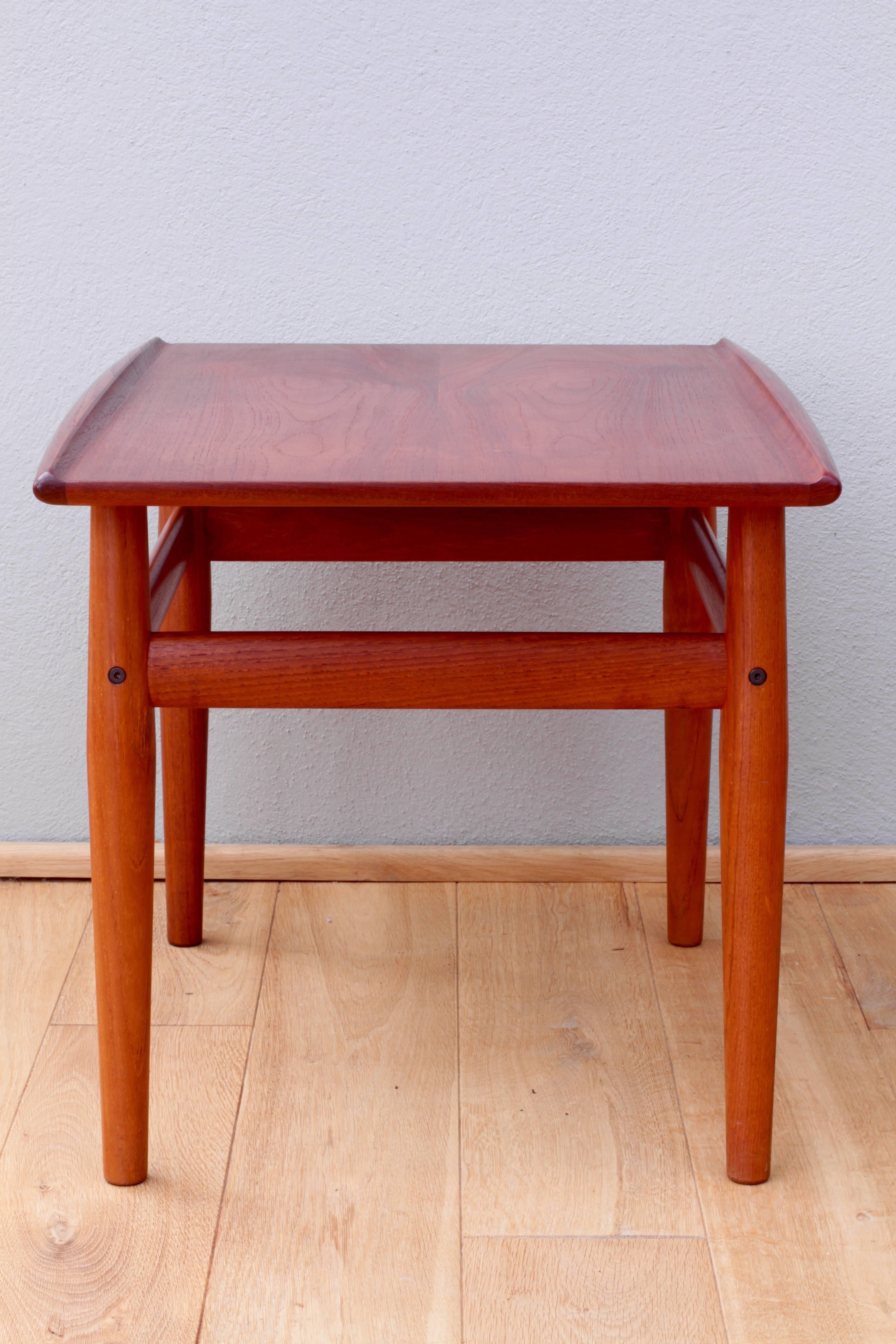 A wonderful vintage Mid-Century side or end table by Grete Jalk for Glostrup Møbelfabrik, made in Denmark, circa 1964. This beautifully constructed solid teak table features elegantly tapered legs, brass details and a hand shaped, lipped tabletop