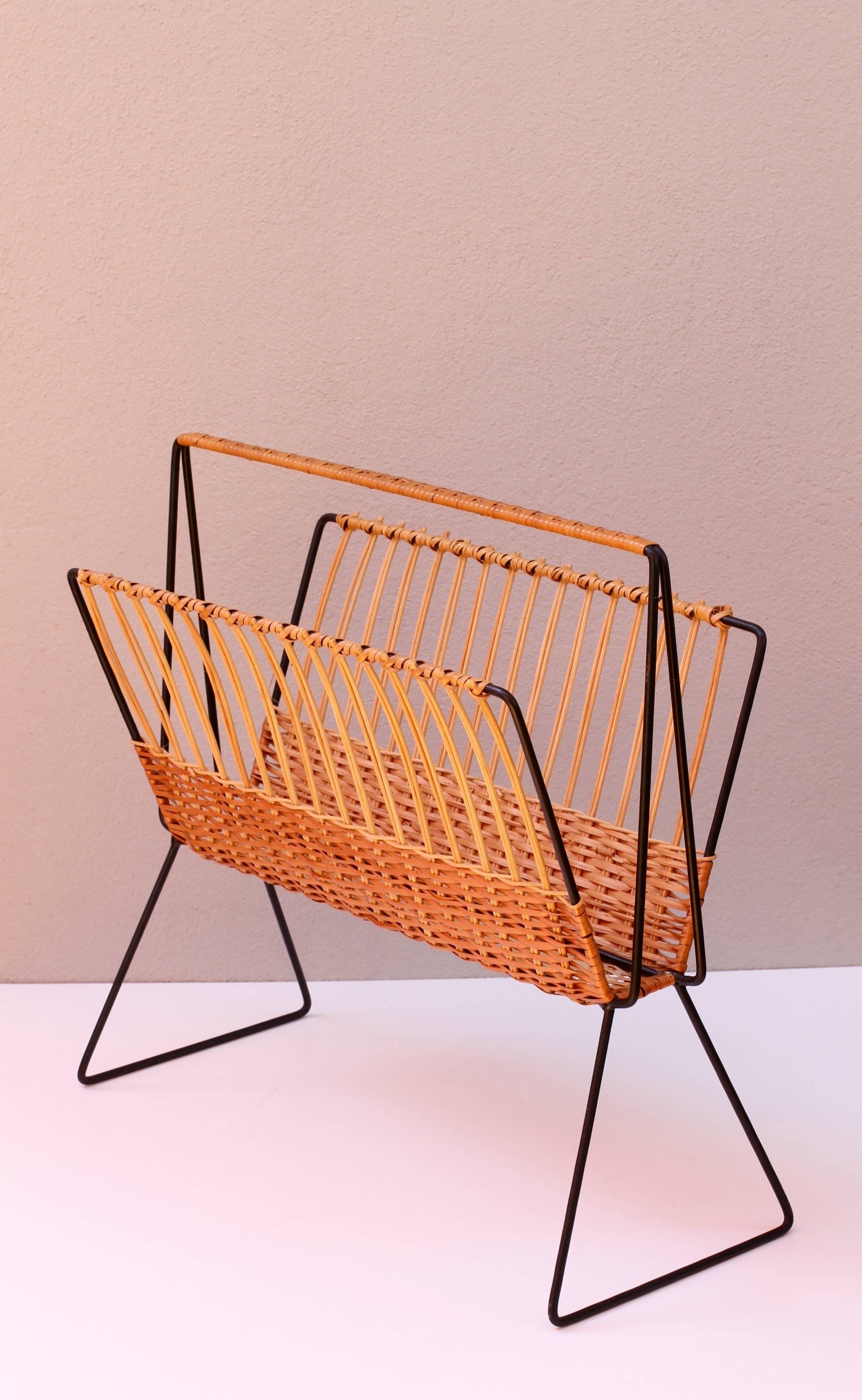 This large, oversized magazine stand or holder, attributed to Austrian Carl Auböck, circa 1950s, features woven wicker / rattan strands which wrap around the black painted steel wire frame creating, what is, a wonderfully minimal, modernist piece of