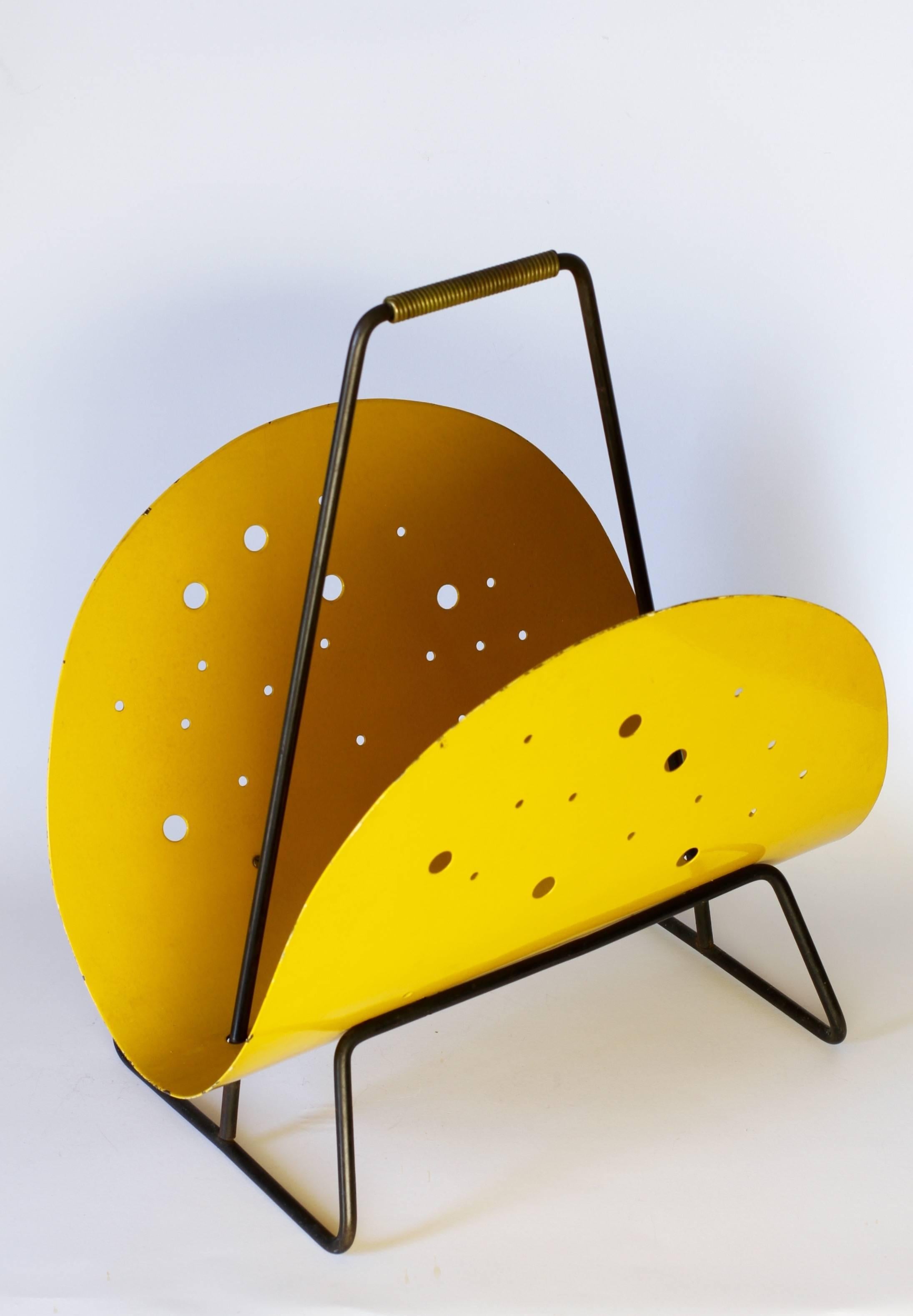 A wonderfully unusual and rare Mid-Century Modernist magazine stand or newspaper holder from the 1950s. Featuring a vibrant yellow painted curved metal holder with perforated holes of different sizes this piece very much reflects the style of both