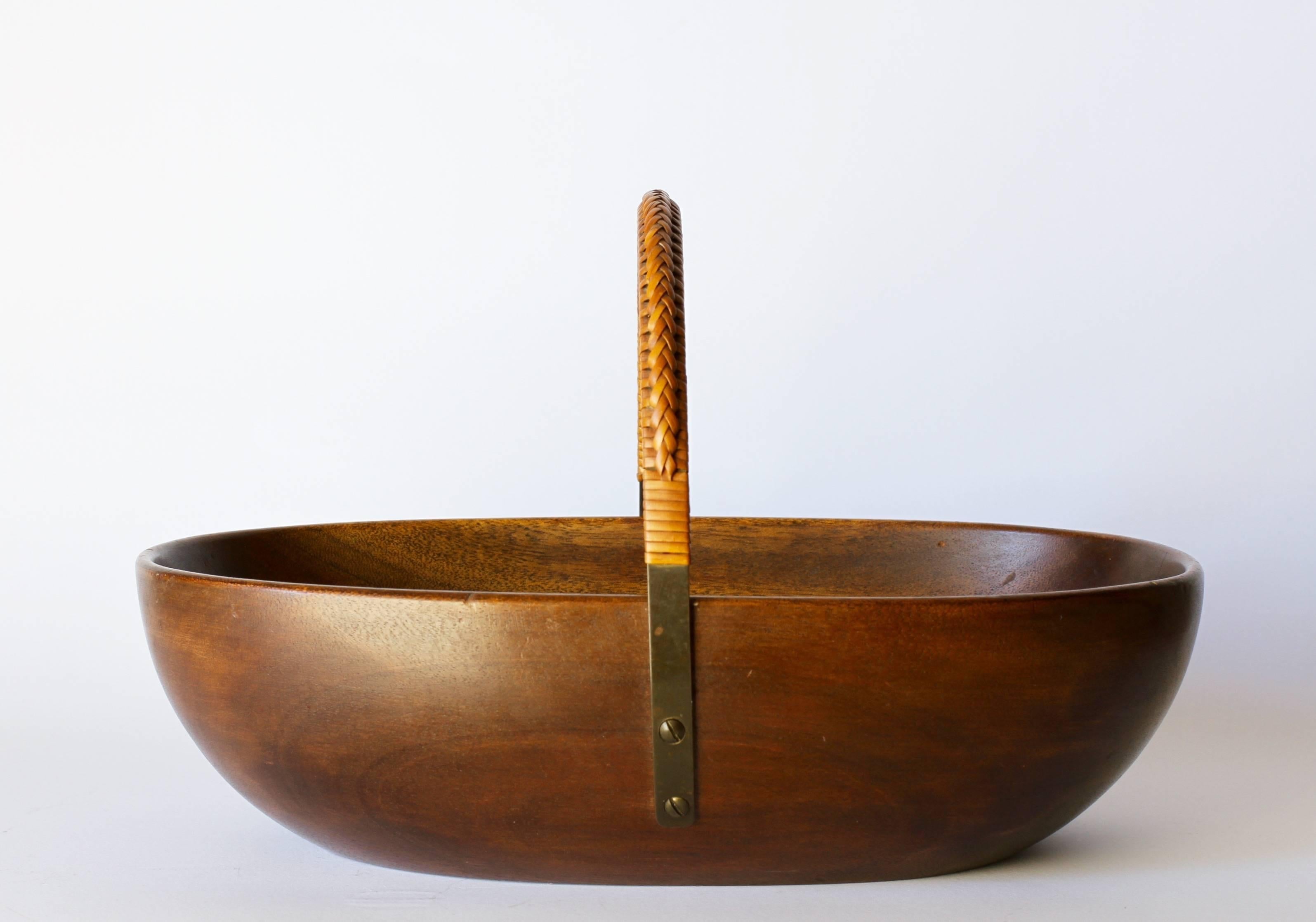 Hand-carved mahogany nut bowl by Carl Auböck, Austria, circa 1955. This beautifully made bowl features a curved brass handle which follows the lines and shape of the bowl with delicately woven or weaved rattan.

Model A-436.