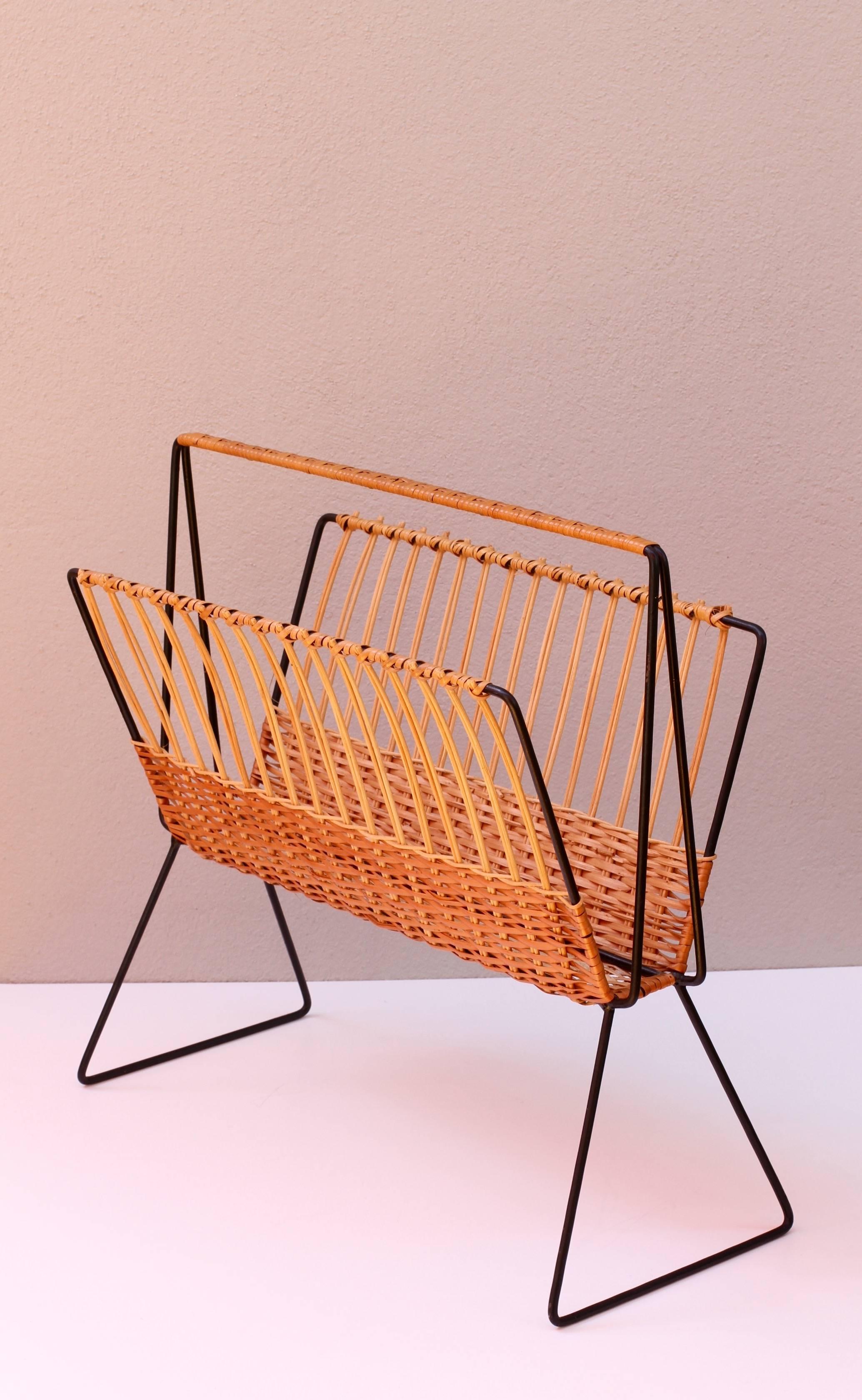 This large, oversized magazine stand or holder, in the style of Rohe Noordwolde, circa 1950s, features woven wicker / rattan strands which wrap around the black painted steel wire frame creating, what is, a wonderfully minimal, modernist piece of