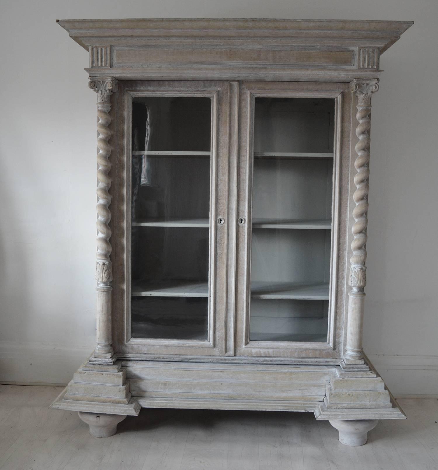 
Wonderful architectural limed oak glazed cabinet.
 
An oversized cornice is reflected in an equally large base or plinth.

Corinthian twisted columns attached to the doors.
 
Fabulous original glass panels.

The piece has been recently