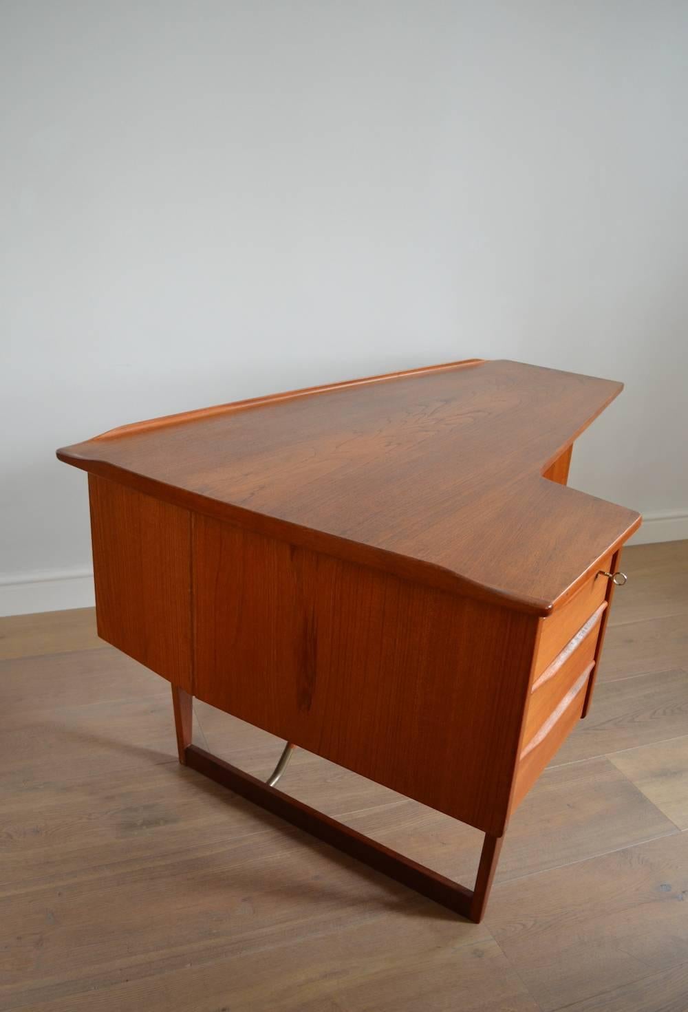 Stunning sculptural teak 'boomerang' desk designed by Peter Løvig Nielsen for Hedensted Møbelfabrik, circa 1956.

Featuring an open bookcase to the rear and a concealed, mirrored drop-down drinks cabinet. Comes with original key.

 