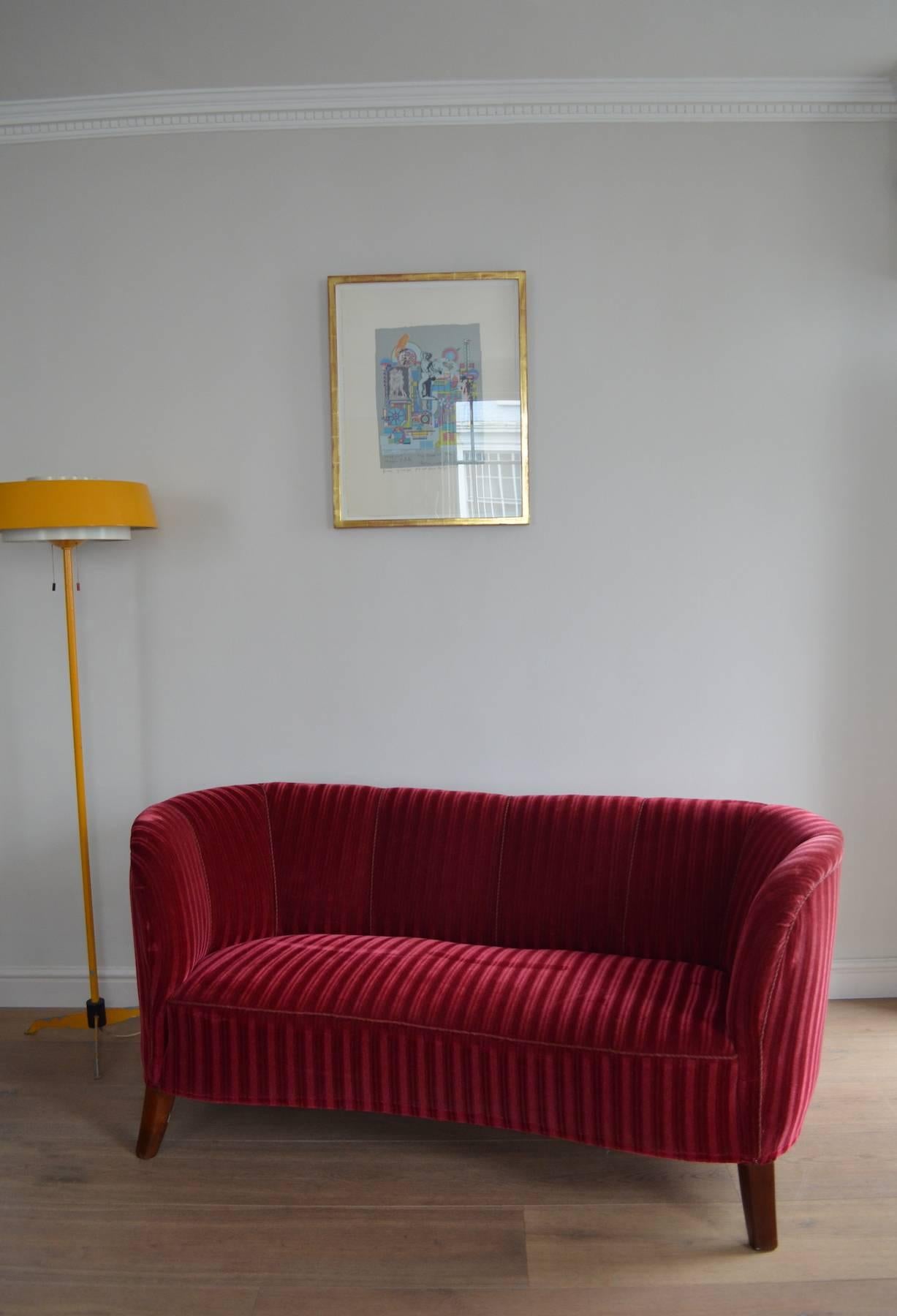 An Art Deco banana sofa with red striped velvet upholstery and piping.