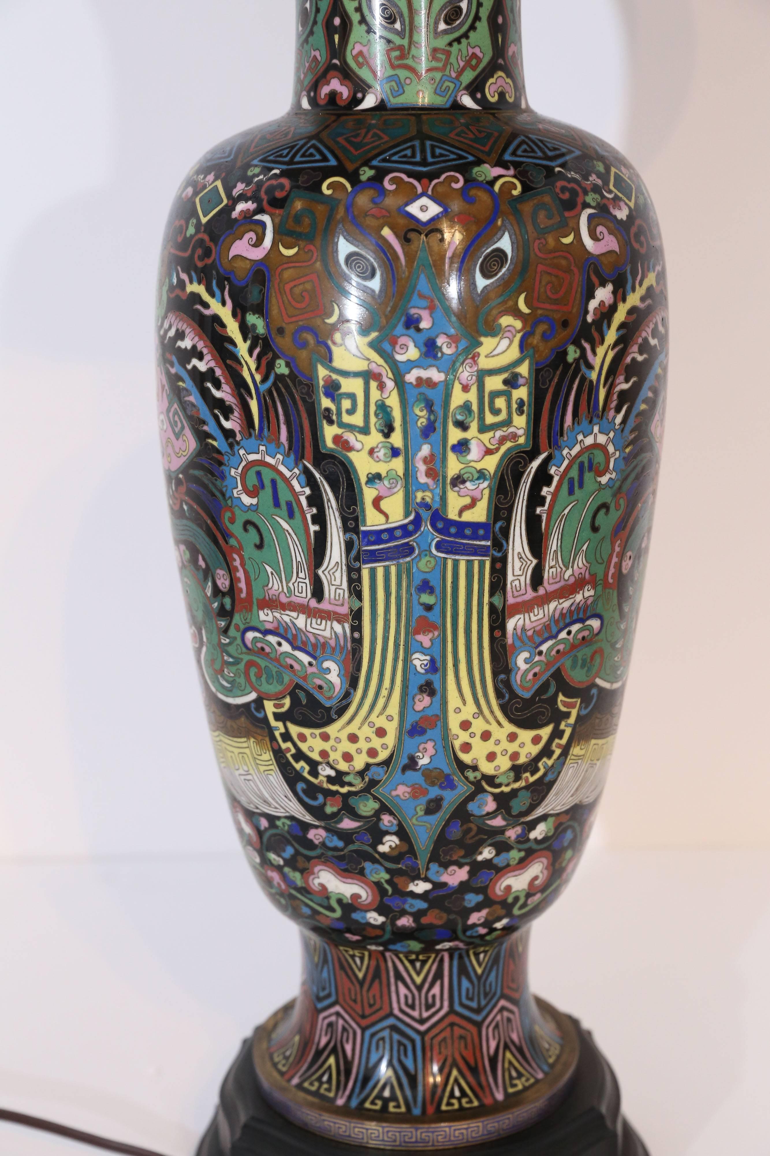 This exquisite cloisonne enameled lamp started its life as a vase. The detailed design of the vase in pastel pink, lavender, red, blue with a black background among others is supported on a carved tiered Stand. Light green carved globe jade finial