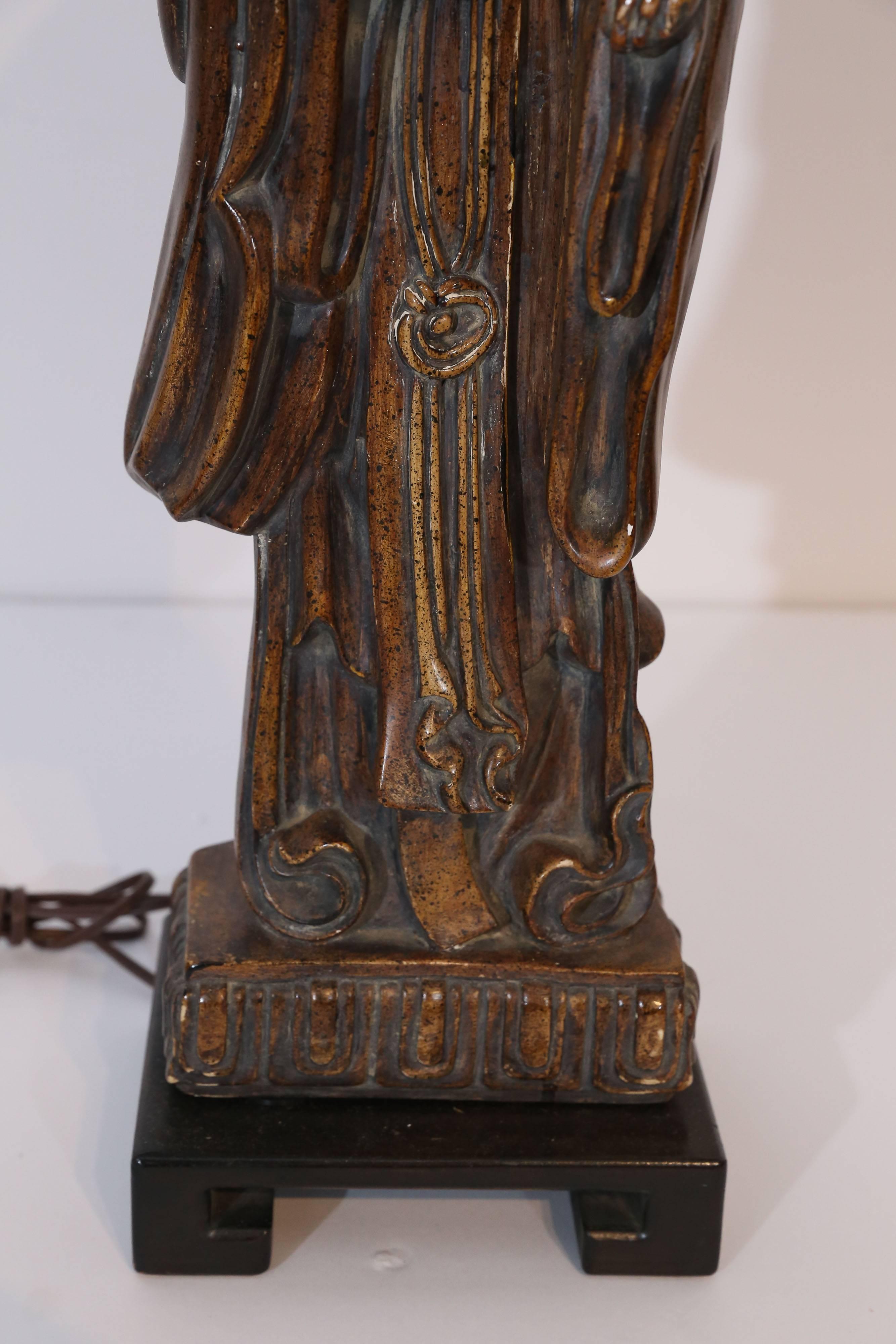 Frederick Cooper resin carved oriental figure sits upon a rectangular base. Painted to resemble a mahogany wood it is distressed bringing out shades of brown and gold. The lamp stands 28.5