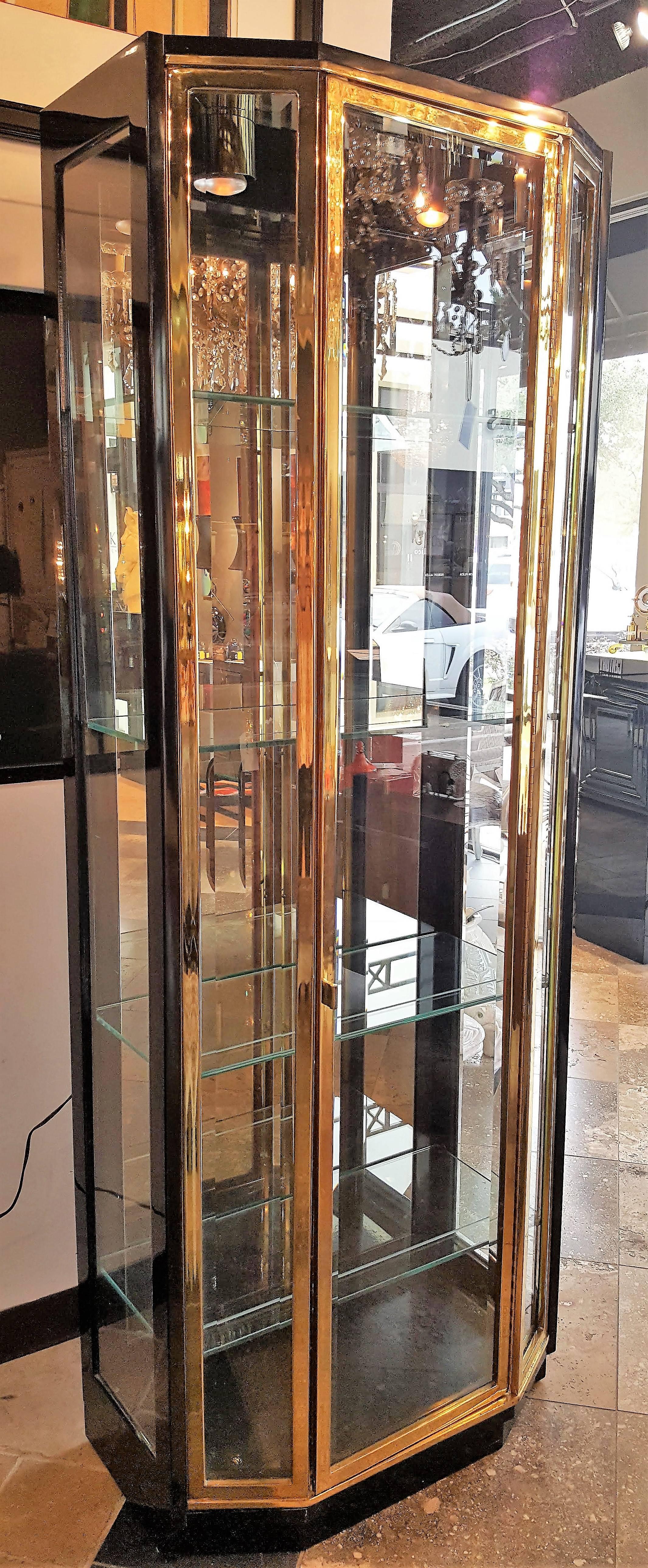 Pair tall 1970s brass display cabinets by Henredon. Beautiful pieces have four rectangular glass shelves, mirrored back wall, and lacquered wooden base. At the inside top of the case are two brass light holders. One door opens on brass hinge. Glass