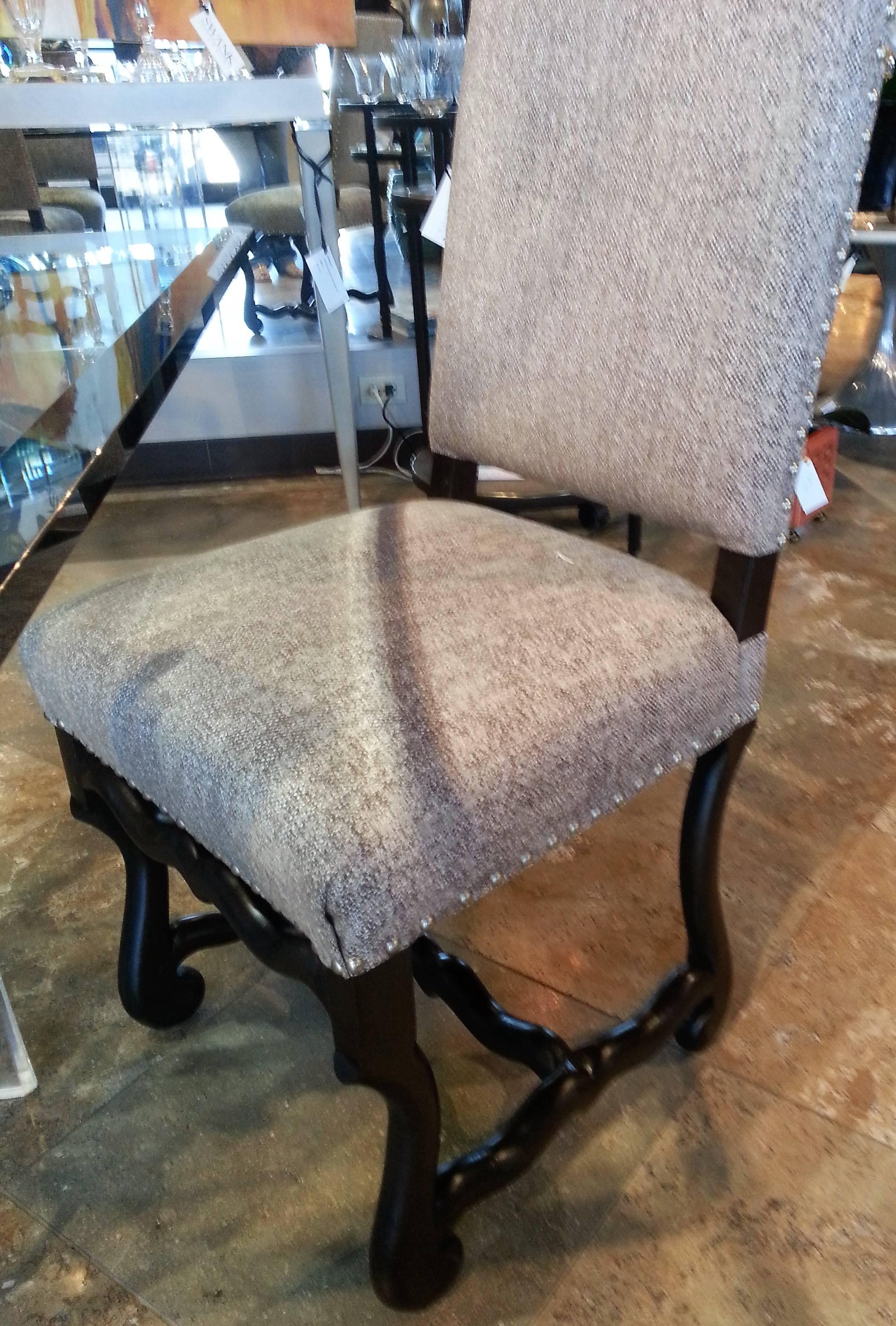 Recently reupholstered in a nubby taupe linen, this set of eight dining room chairs styled in the Jacobean period are finished in an ebony walnut finish. Silver nailhead trim runs along the perimeter of the chairs. Graceful curves accentuate the
