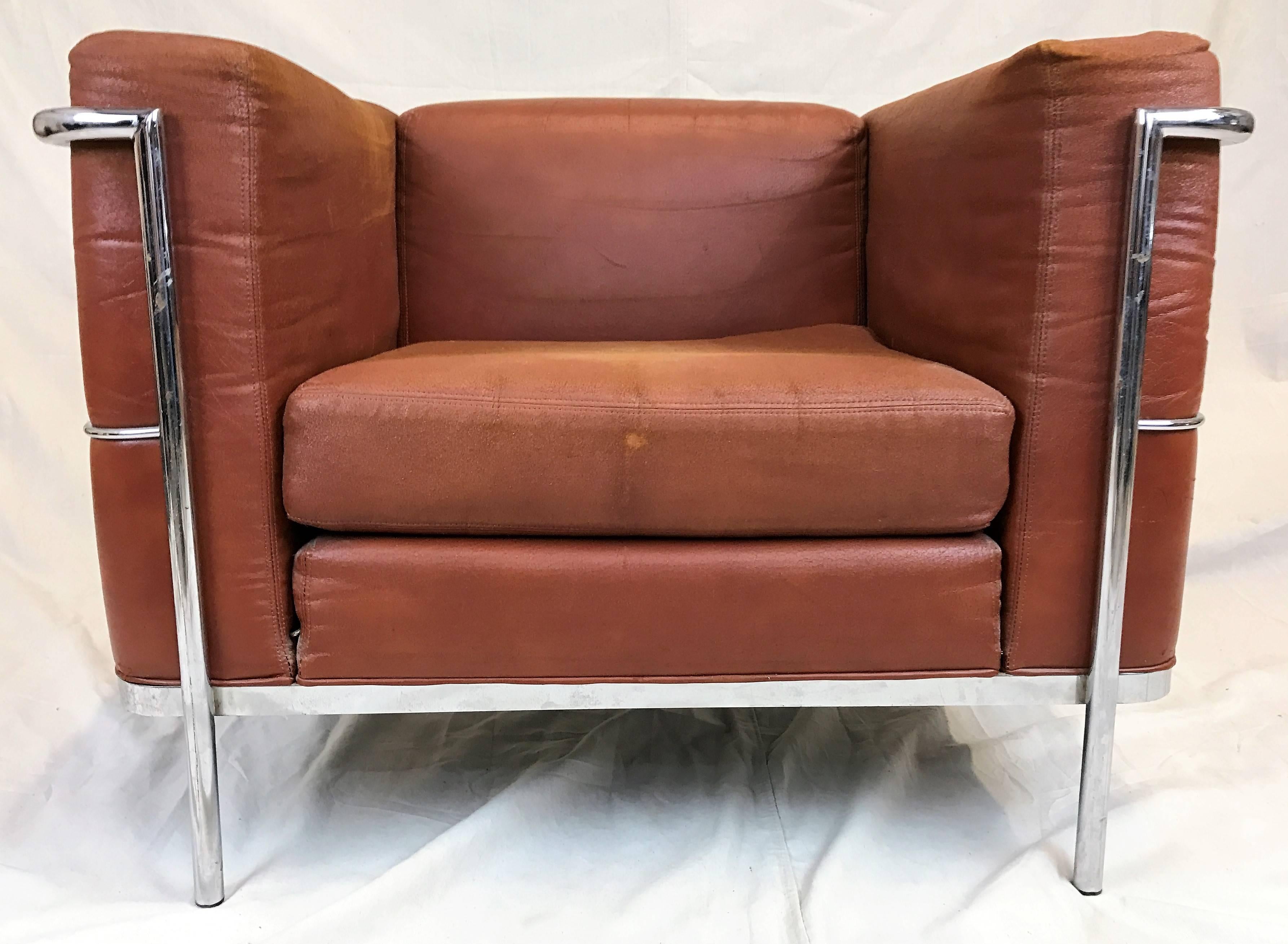 Pair of Mid-Century Modern lounge chairs in an upholstered rust-colored faux leather by Jack Cartwright, circa 1970s, in the manner of the LC2 by Le Corbusier. The original fabric shows some age appropriate wear, some rips in fabric.
