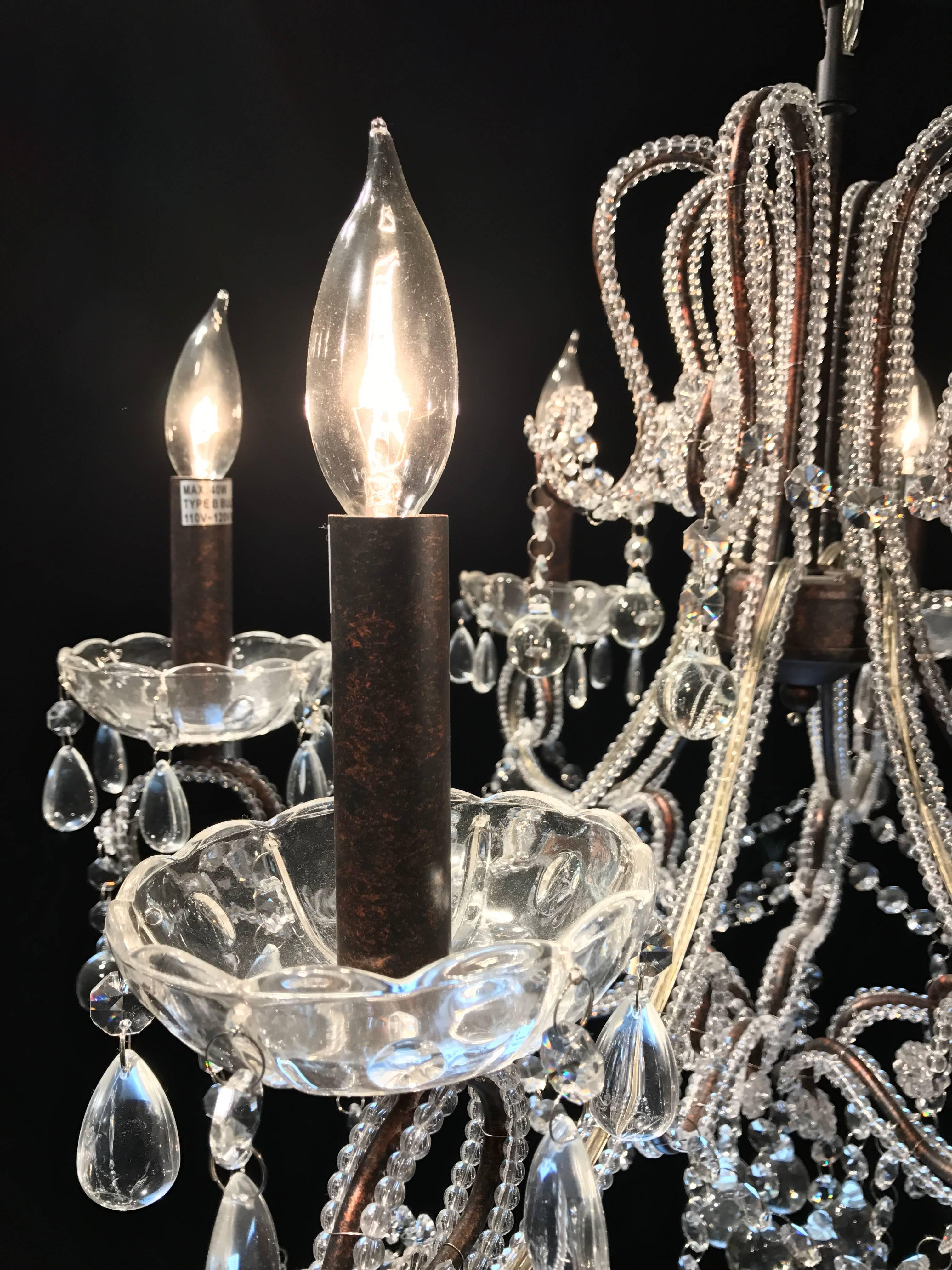 Lovely cut-glass six-arm chandelier festooned with beads from top to bottom and covering the gold colored wiring. Clear pear and glass ball prisms hang from the beading. Bronze sockets perch upon simple bobeches also festooned with hanging teardrop