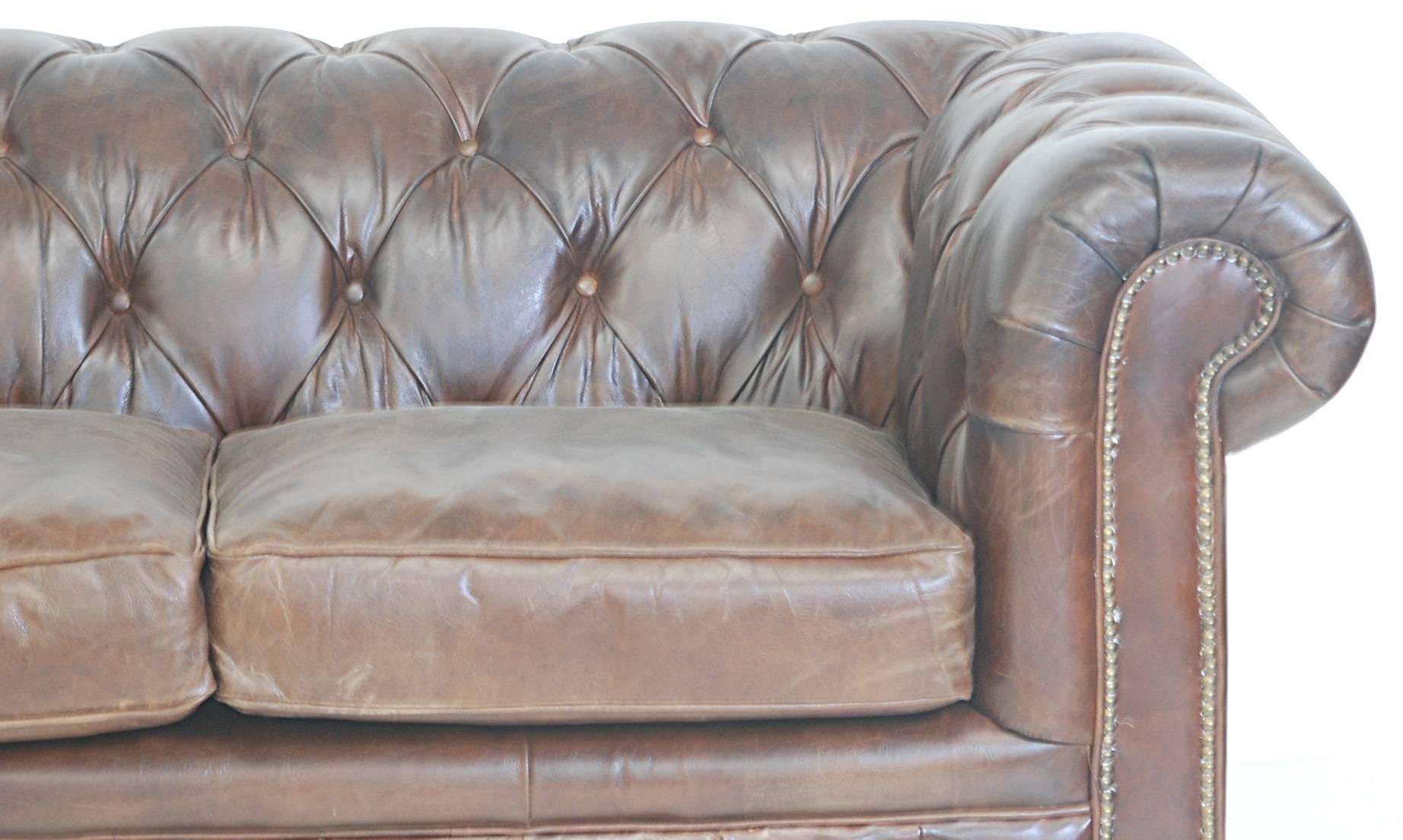 Brown tufted leather with buttons and two loose cushions. Mahogany legs on brass cup casters.