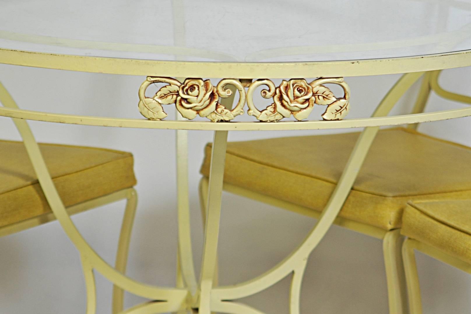 Five-piece wrought iron dining/patio set. Yellow painted with a floral design. One table and four chairs with vinyl upholstery. The table is 42 inches in diameter and 28.75 inches high. Chair dimensions are below.