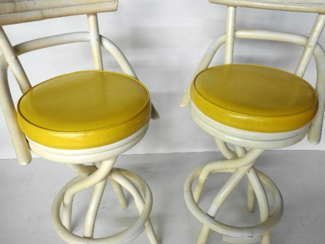 Pair of James Mont style barstools by Hermosa Rattan with distressed yellow paint and yellow vinyl upholstery.