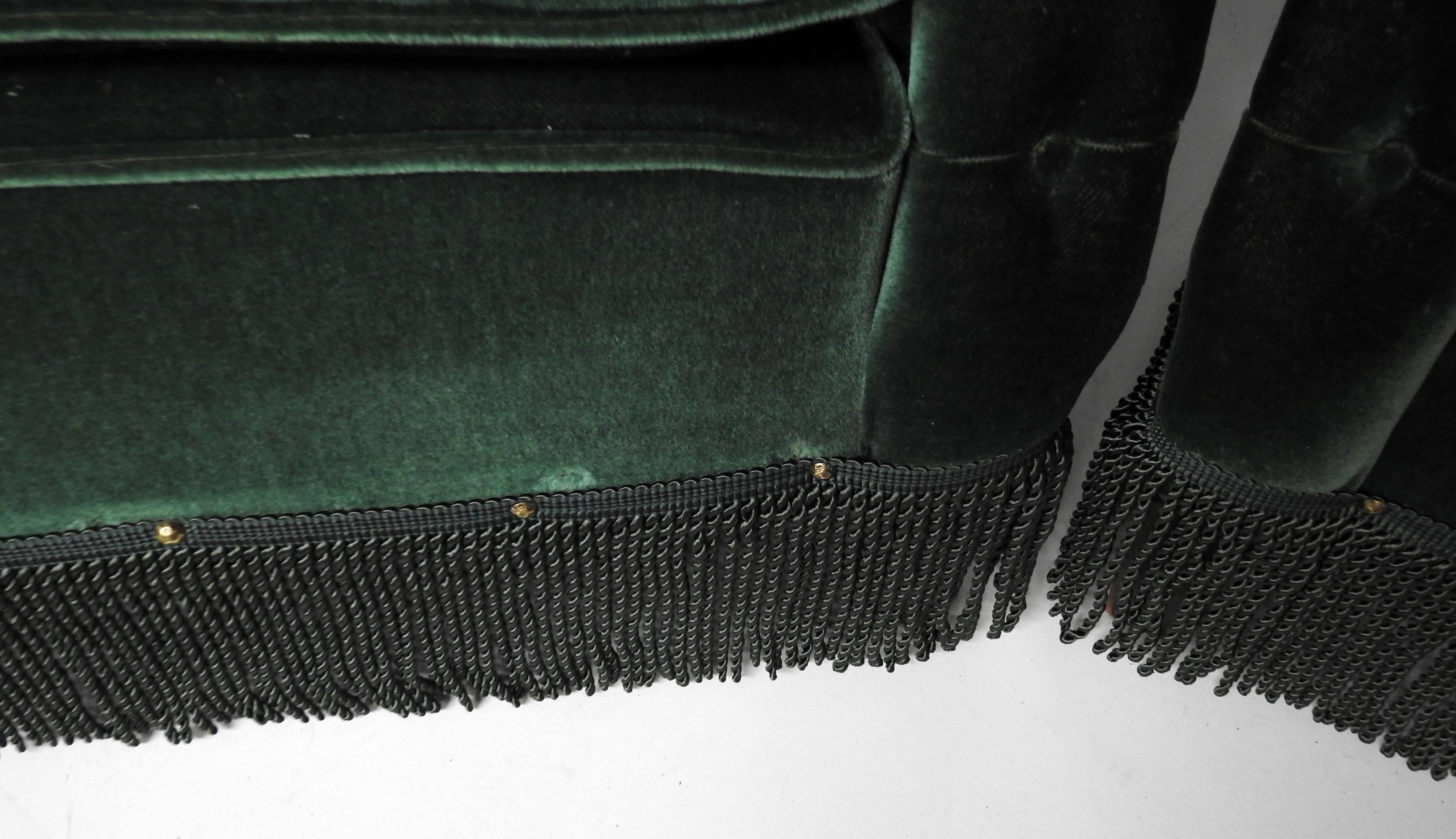 Pair of Hollywood Regency tufted club chairs with nailhead trim and fringe skirting.