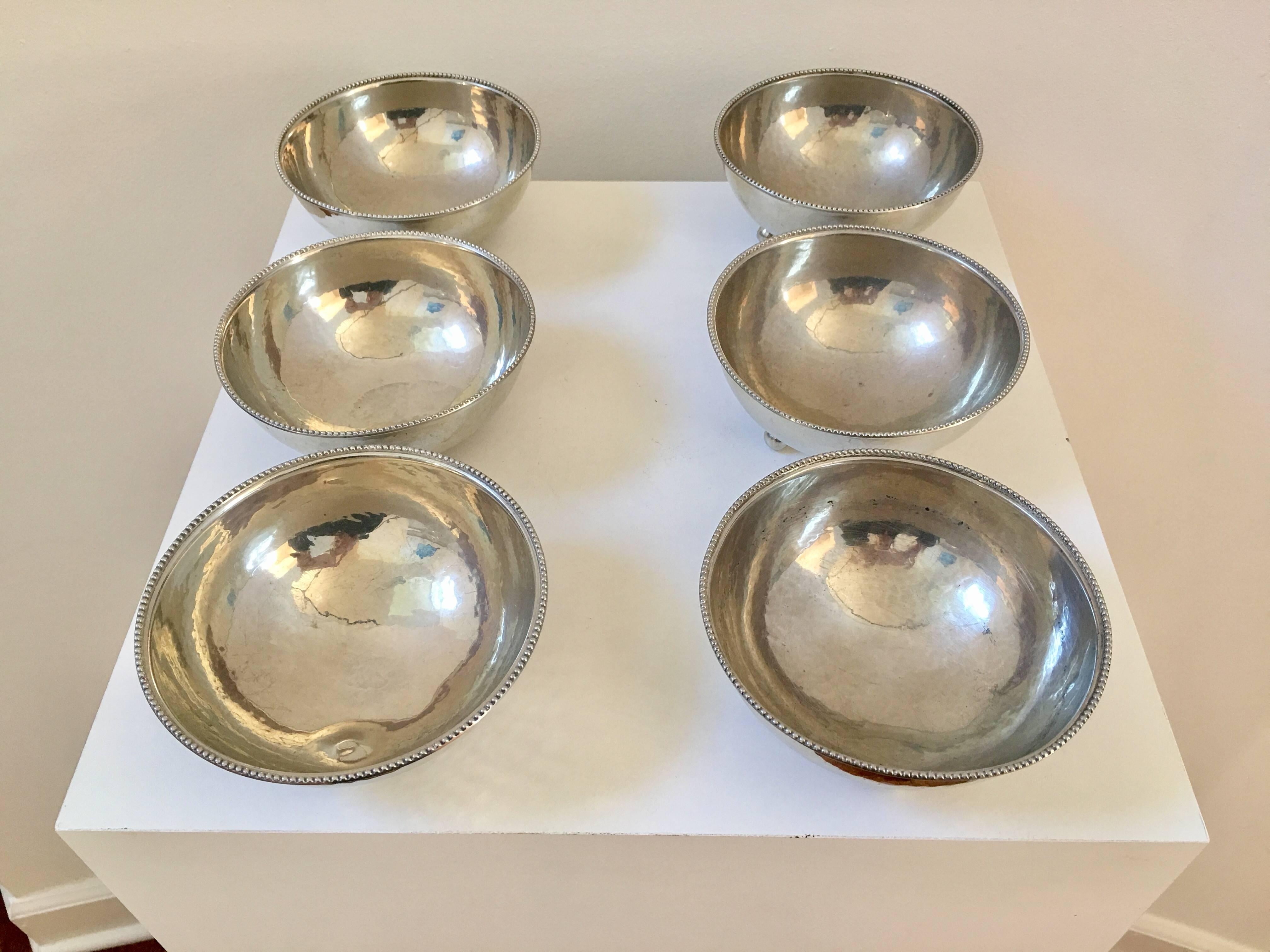 A fabulously detailed set of six pewter bowls with an almost silver finish. Each bowl size and curvature fits the palm of your hand beautifully while the three ball feet in each bowl rests easy on a table. The beading detail on the rim of each bowl