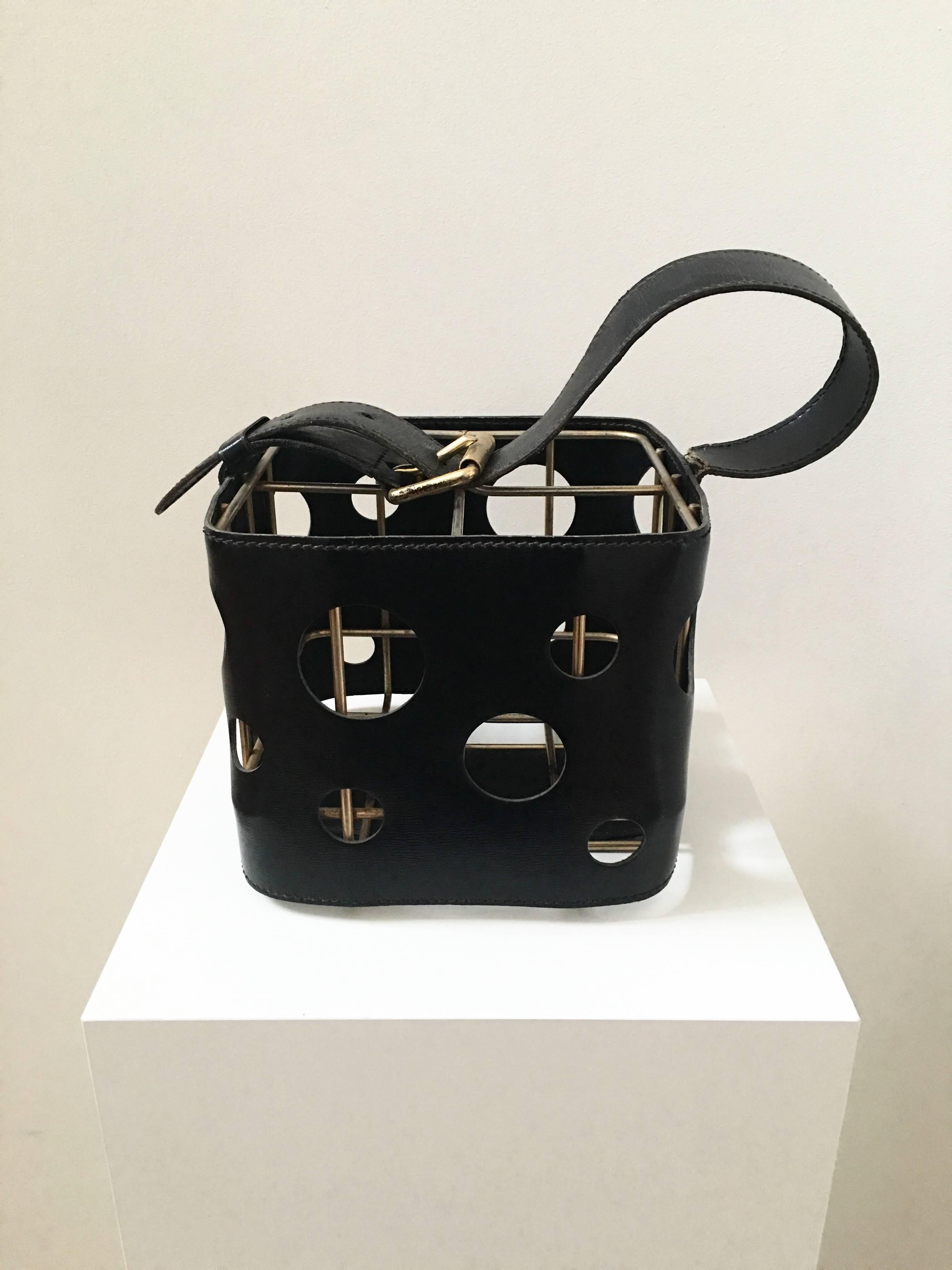 Uber stylish black leather caddy for wine/bottles is attributed to Jacques Adnet (1901-1984). Holes of varying sizes are created on the black leather that wraps a brass frame. The leather belt and brass buckle add a nice touch to this piece. Perfect