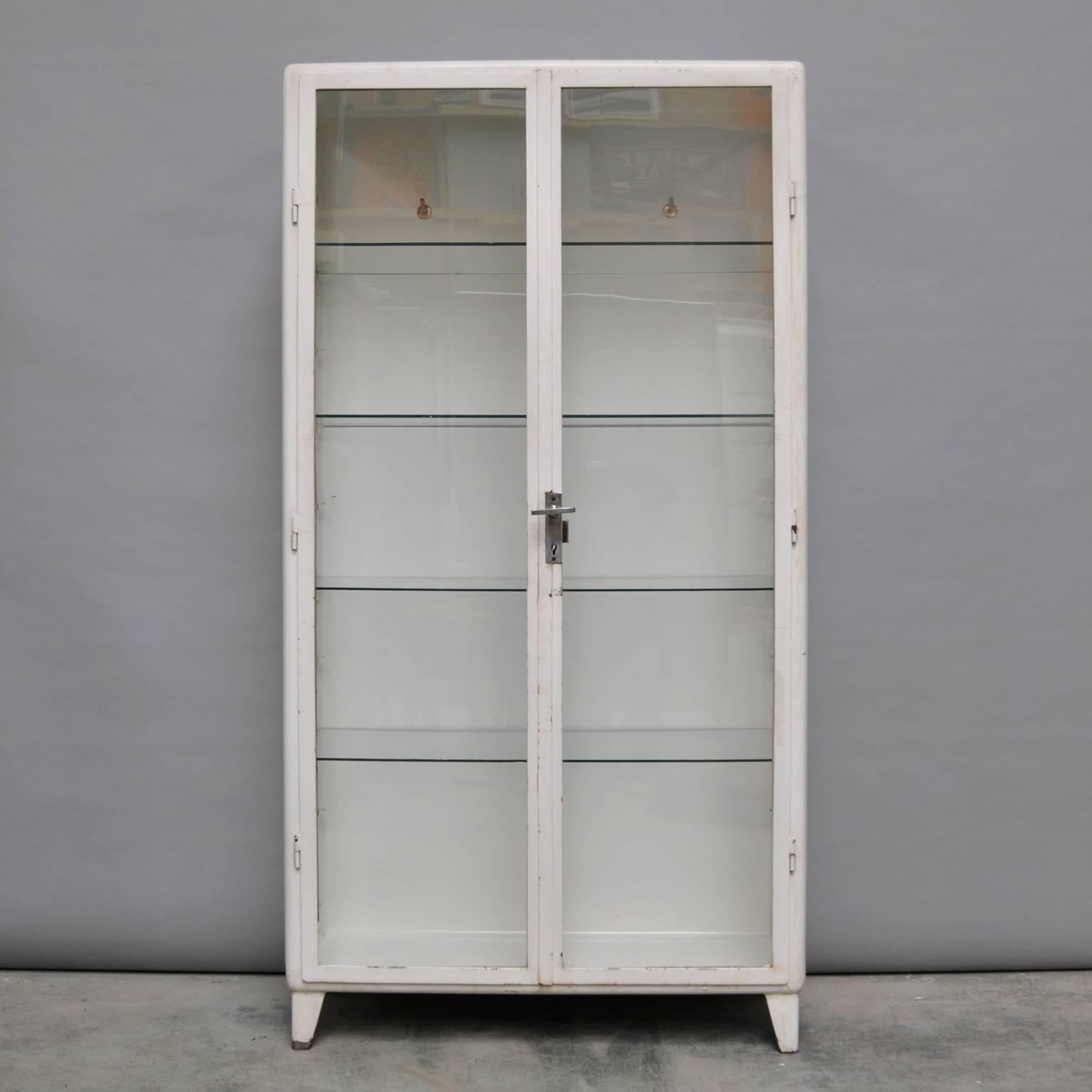 This vintage cabinet was produced in Poland during the 1950s. The cabinet is made of steel and comes with four glass shelves. The glass of the cabinet is antiqued. The inside of the cabinet features three clothing hooks.