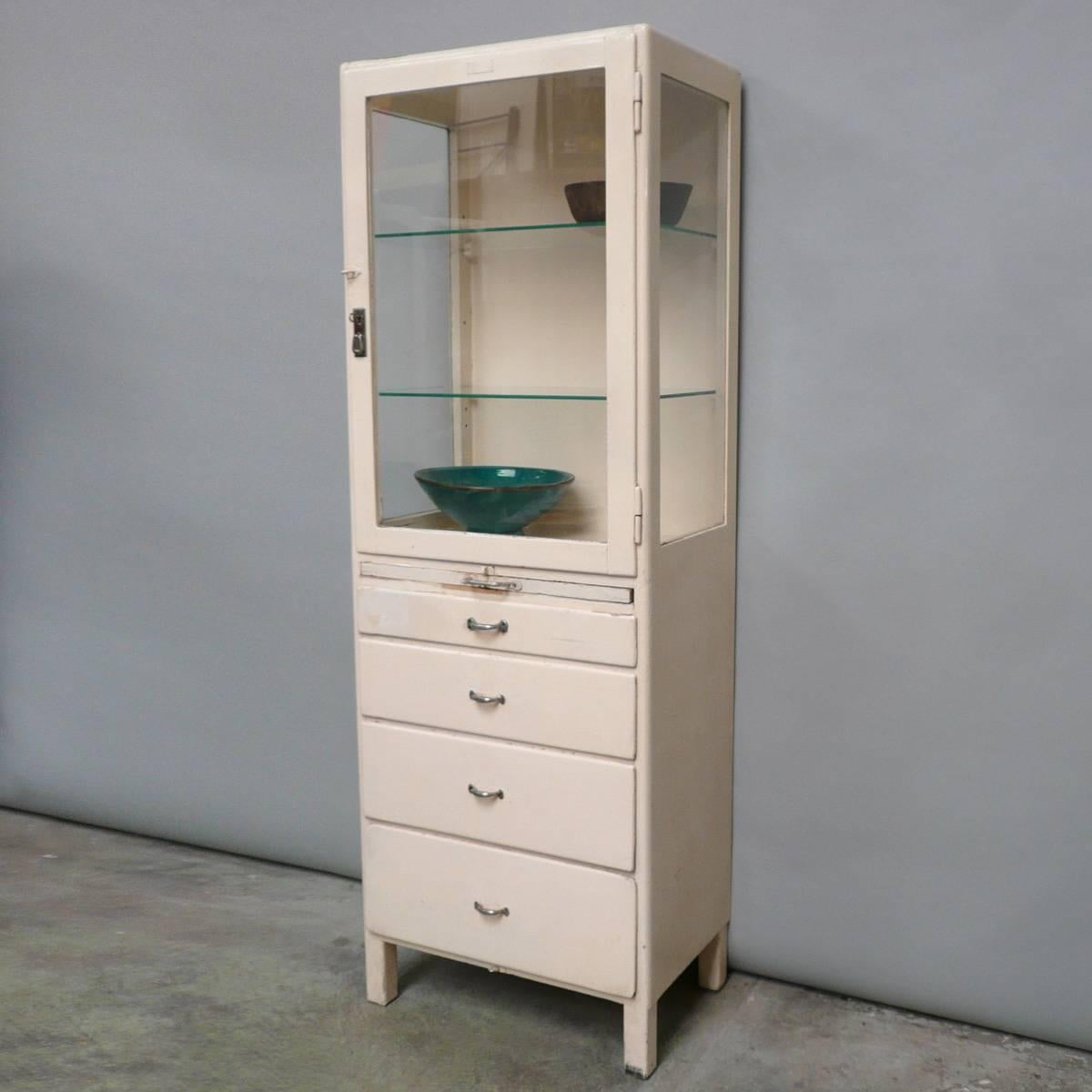 Charming wooden medical cabinet from the 1940s. With the original antique, beveled glass. Produced in Hungary. In the upper part two glass shelves. Below four drawers and a pull-out glass shelf.