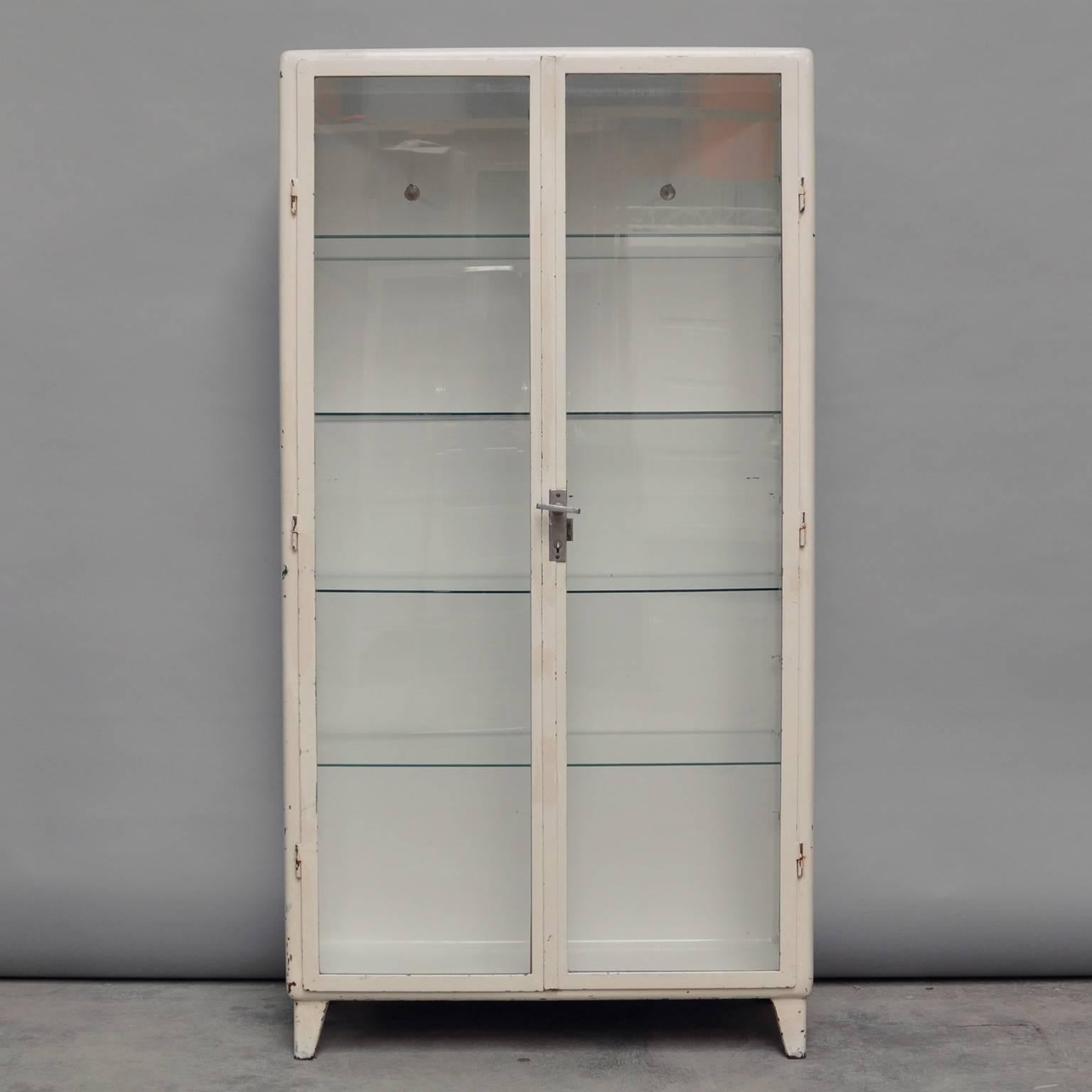 This vintage cabinet was produced in Poland during the 1950s. The cabinet is made of steel and comes with four glass shelves. The glass of the cabinet is antiqued. The inside of the cabinet features three clothing hooks.