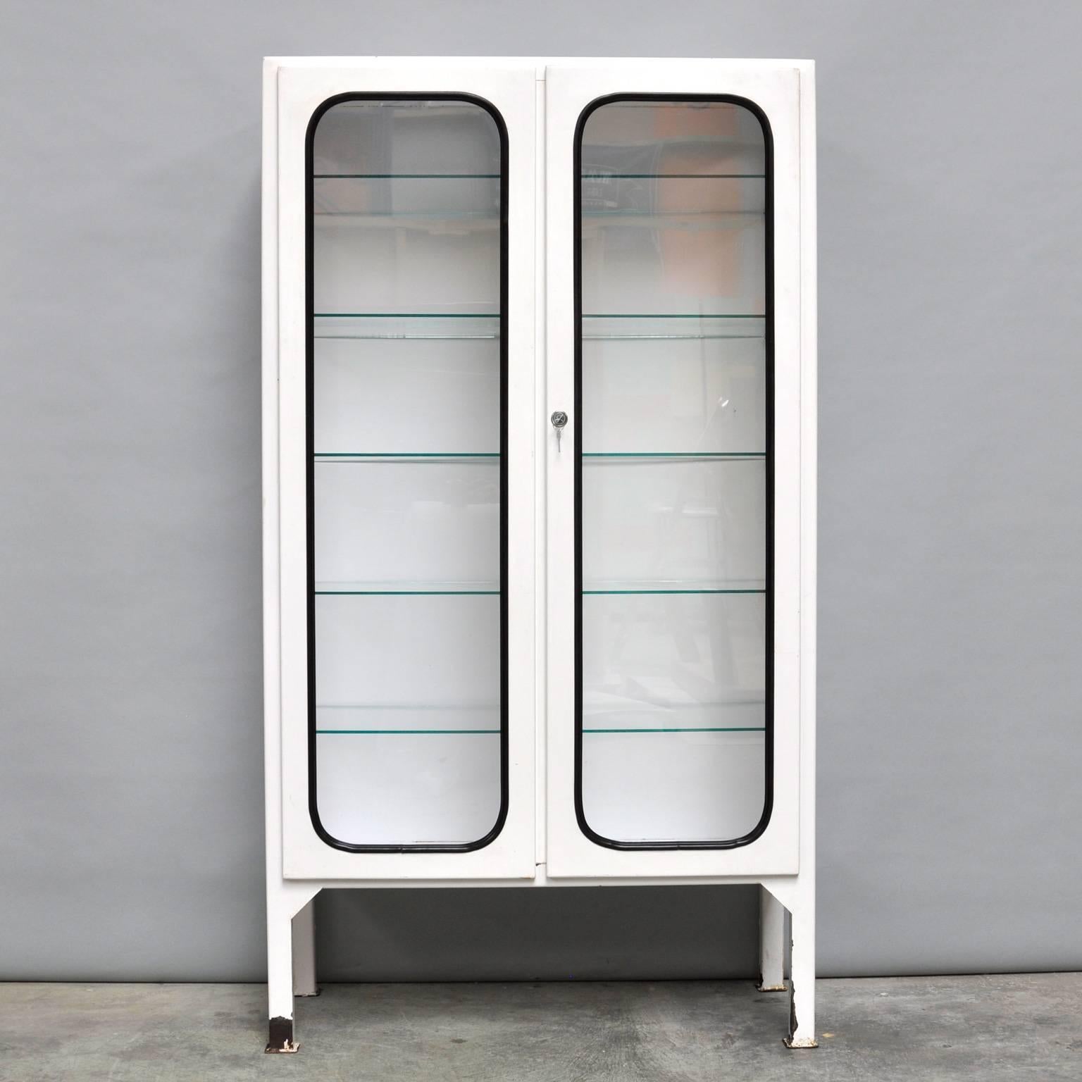 This medicine cabinet was designed in the 1960s and produced in the 1970s in Hungary. It is made of steel and glass. The glass is held by a black rubber strip. The cabinet comes with five adjustable glass shelves and a functioning lock. It is in