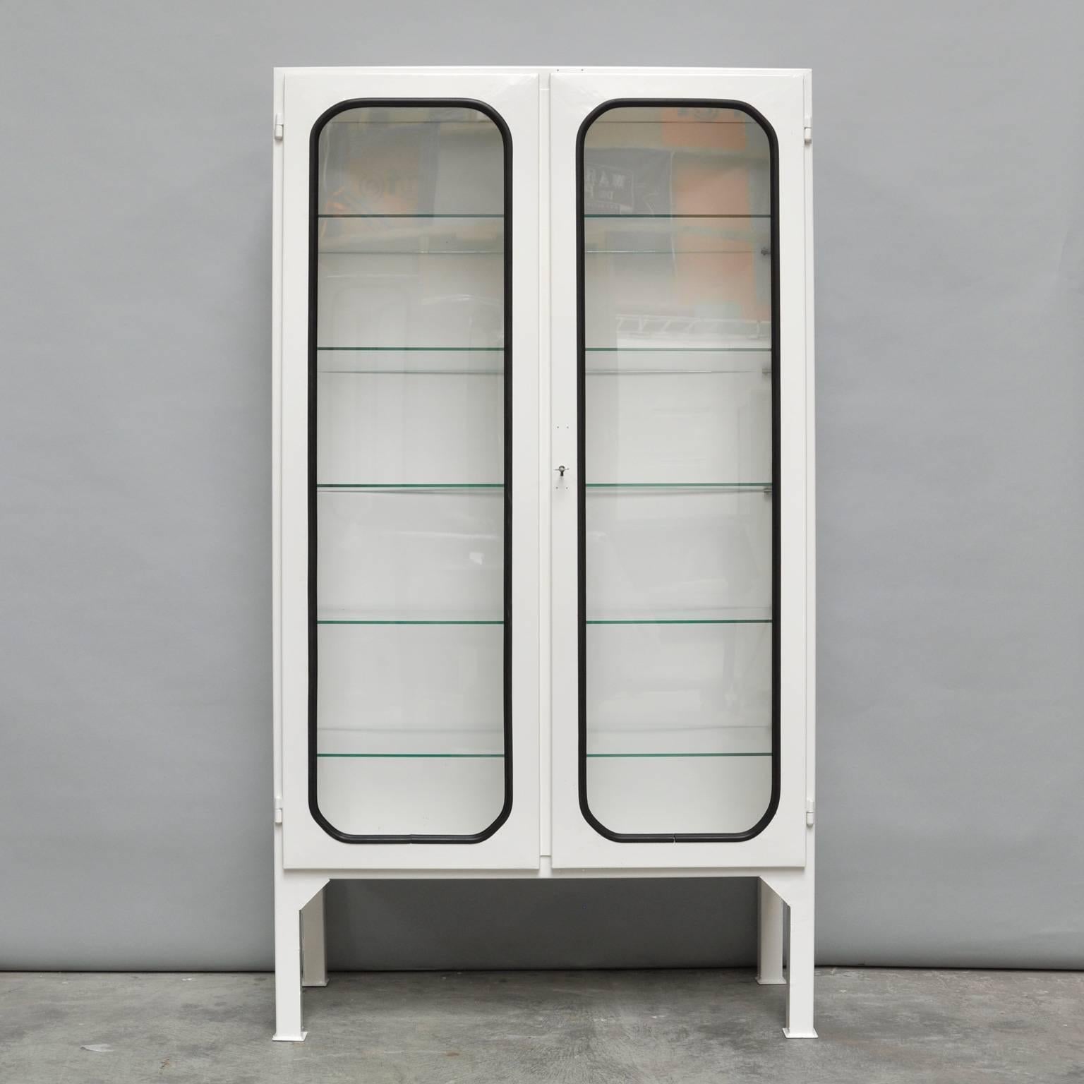 This medicine cabinet was designed in the 1970s and produced, circa 1975 in Hungary. It is made of steel and antique glass. The glass is held by a black rubber strip. The cabinet comes with five (new) adjustable glass shelves and a functioning lock.