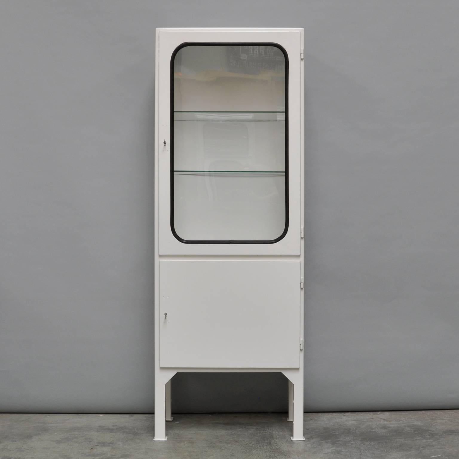 This medicine cabinet was designed in the 1960s and produced in the 1970s in Hungary. It is made from steel and antique glass and the glass is held by a black rubber strip. The cabinet comes with two (new) adjustable glass shelves and functioning