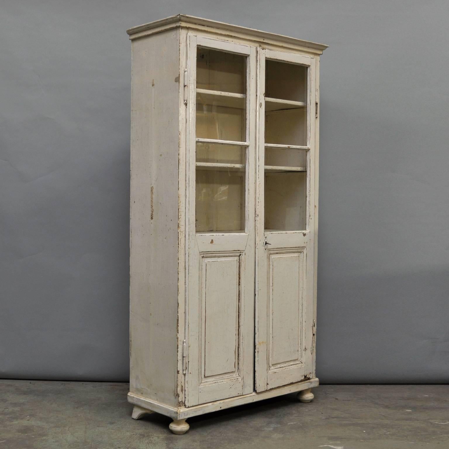 This cabinet was manufactured early in the 20th century. It is made from wood, featuring two glass display windows, two swinging doors and shelves within the interior. The display cabinet has been polished and is in a very good antique condition