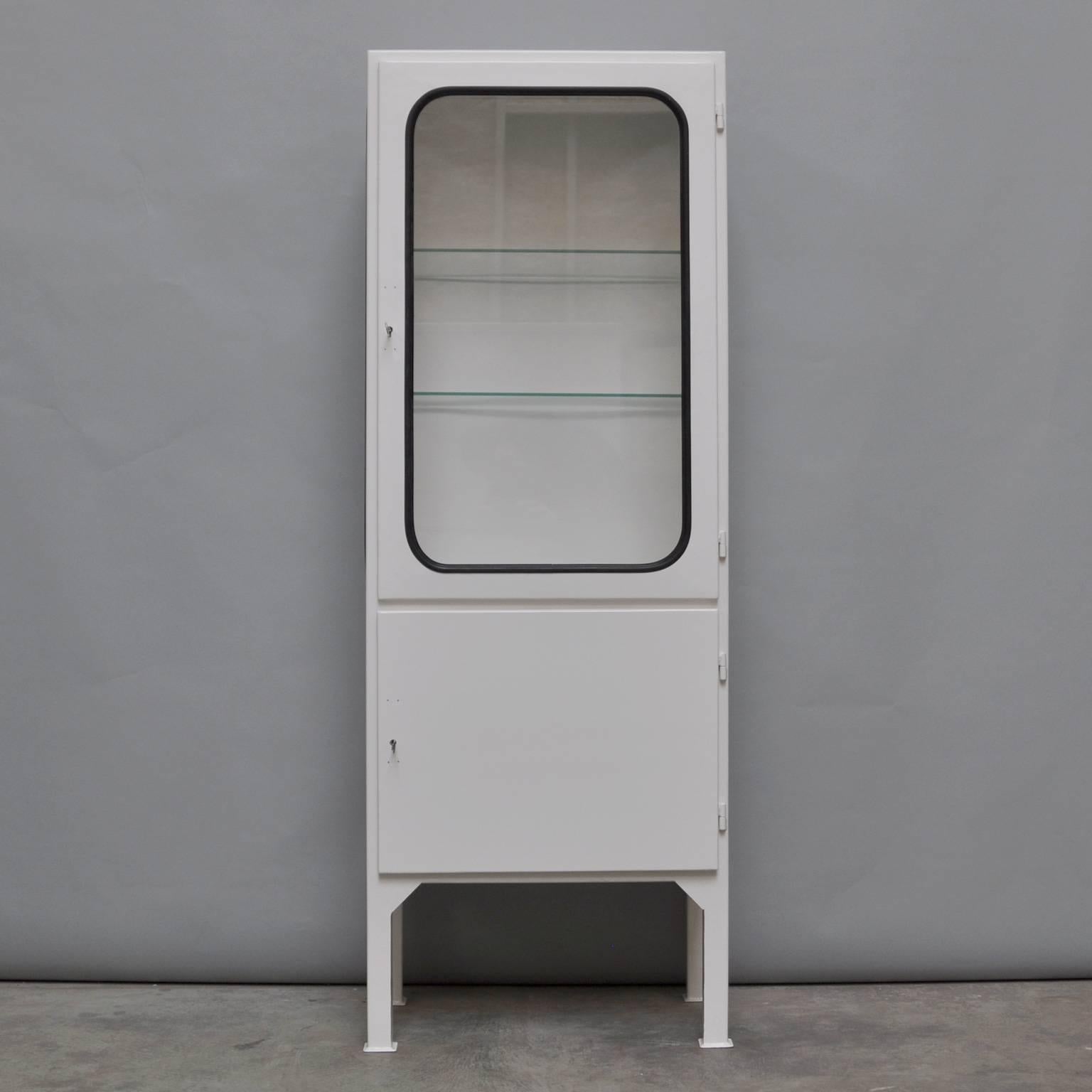 This medicine cabinet was designed in the 1970s and produced, circa 1975 in Hungary. It is made of steel and glass. The glass is held by a black rubber strip. The cabinet comes with two (new) adjustable glass shelves and a functioning lock. The