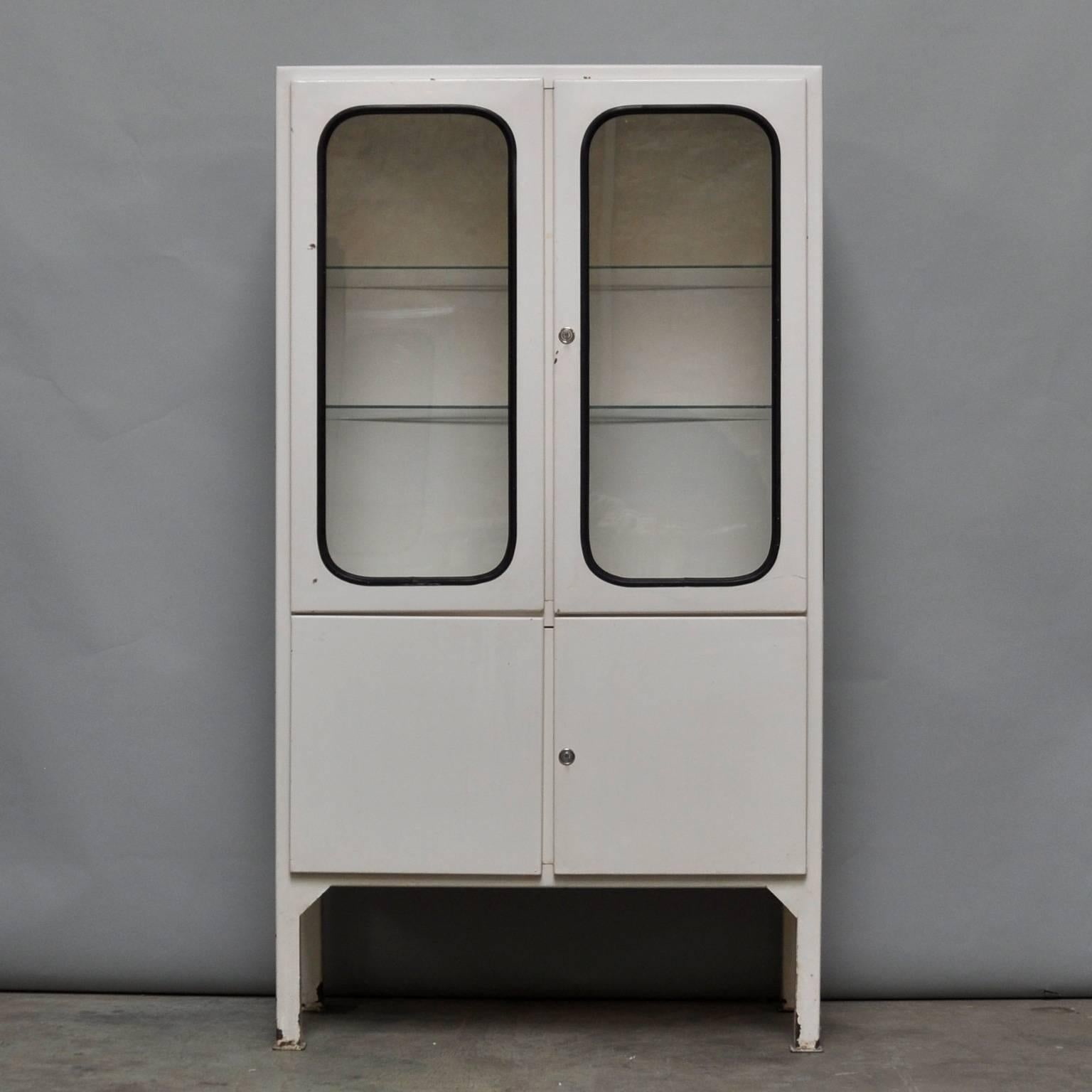 This medicine cabinet was designed in the 1970s and was produced circa 1975 in Hungary. The piece is made from iron and antique glass and the glass is held by a black rubber strip. The cabinet features two adjustable glass shelves and functioning