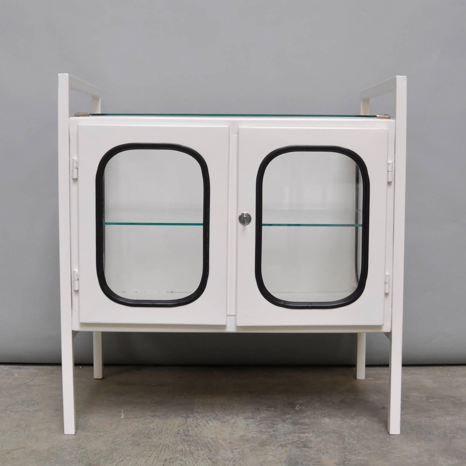This medicine cabinet was designed in the 1970s and was produced, circa 1975 in Hungary. The piece is made from iron and antique glass and the glass is held by a black rubber strip. The cabinet features one glass shelves and a functioning lock.