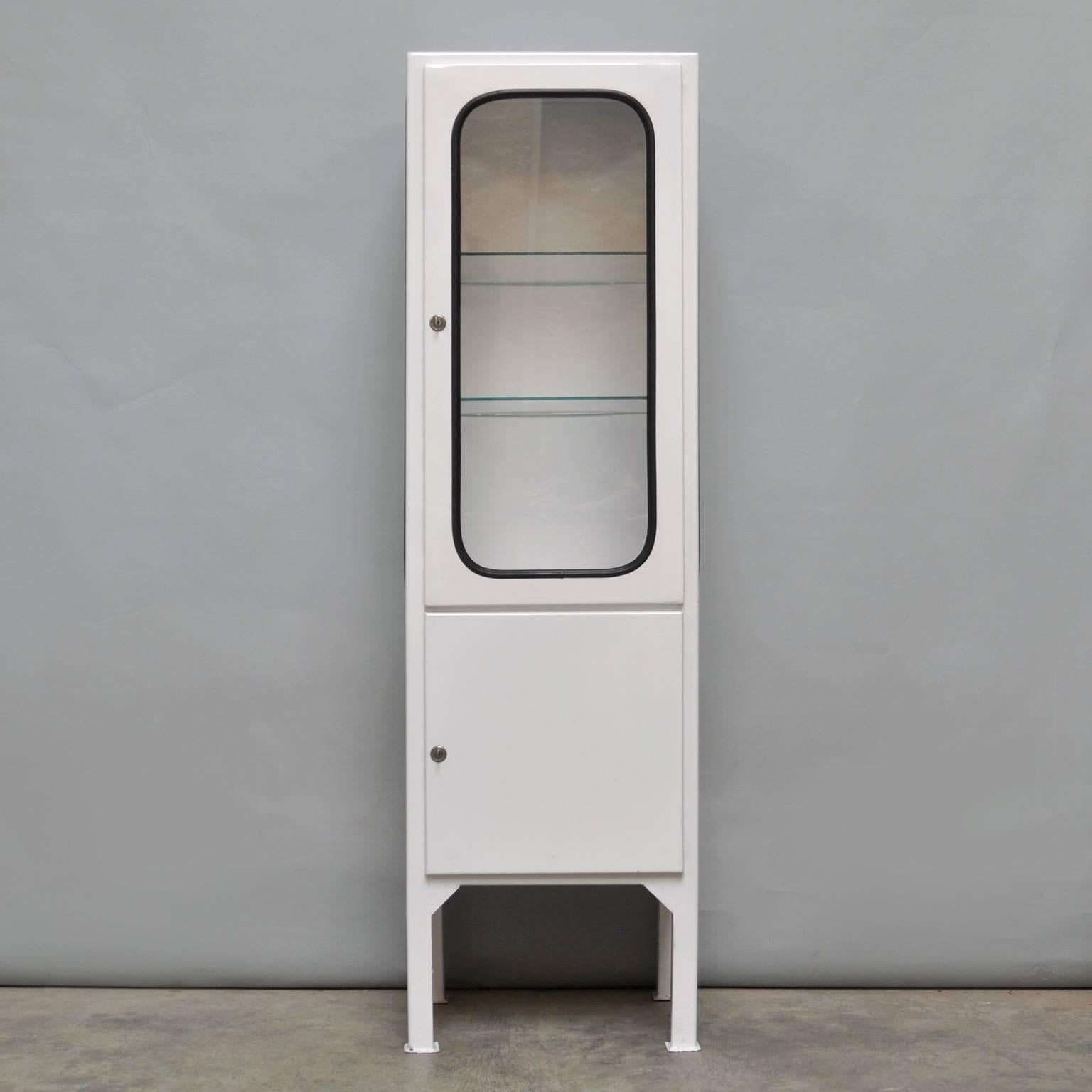 This medicine cabinet was designed in the 1970s and produced in 1975 in Hungary. It is made from steel and glass, with the glass panes held in place by a black rubber strip. The cabinet features two adjustable glass shelves and a functioning locks.